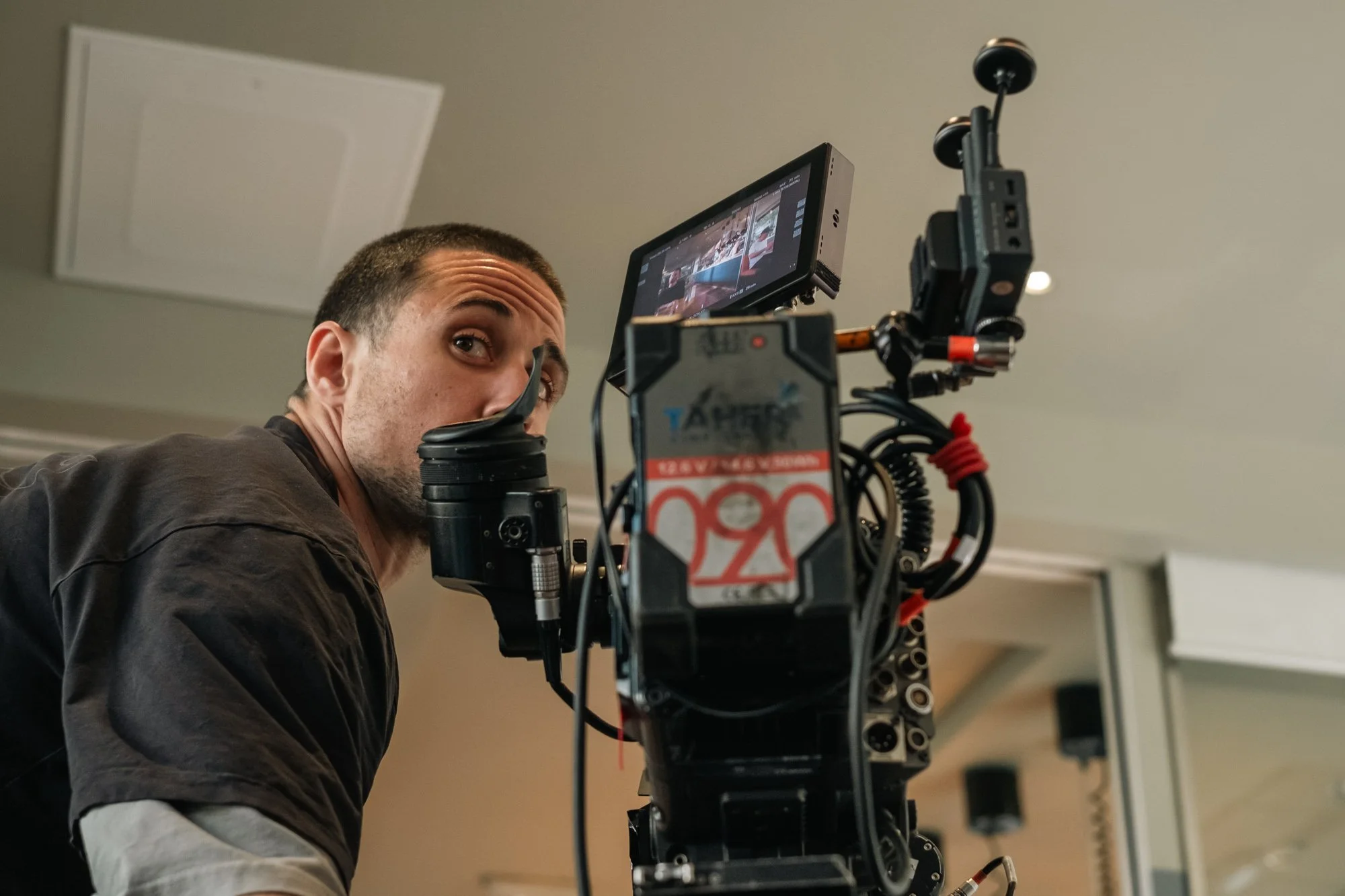 A man looking into a professional video camera setup indoors.