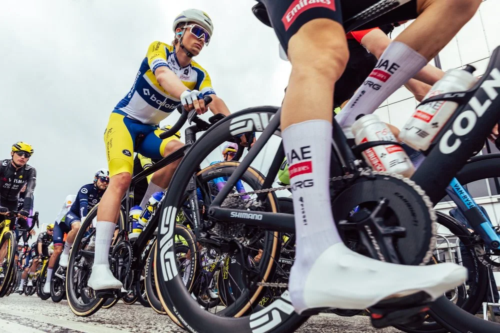 Cyclists at the starting line of a race, viewed from a low angle focusing on their bikes and legs.