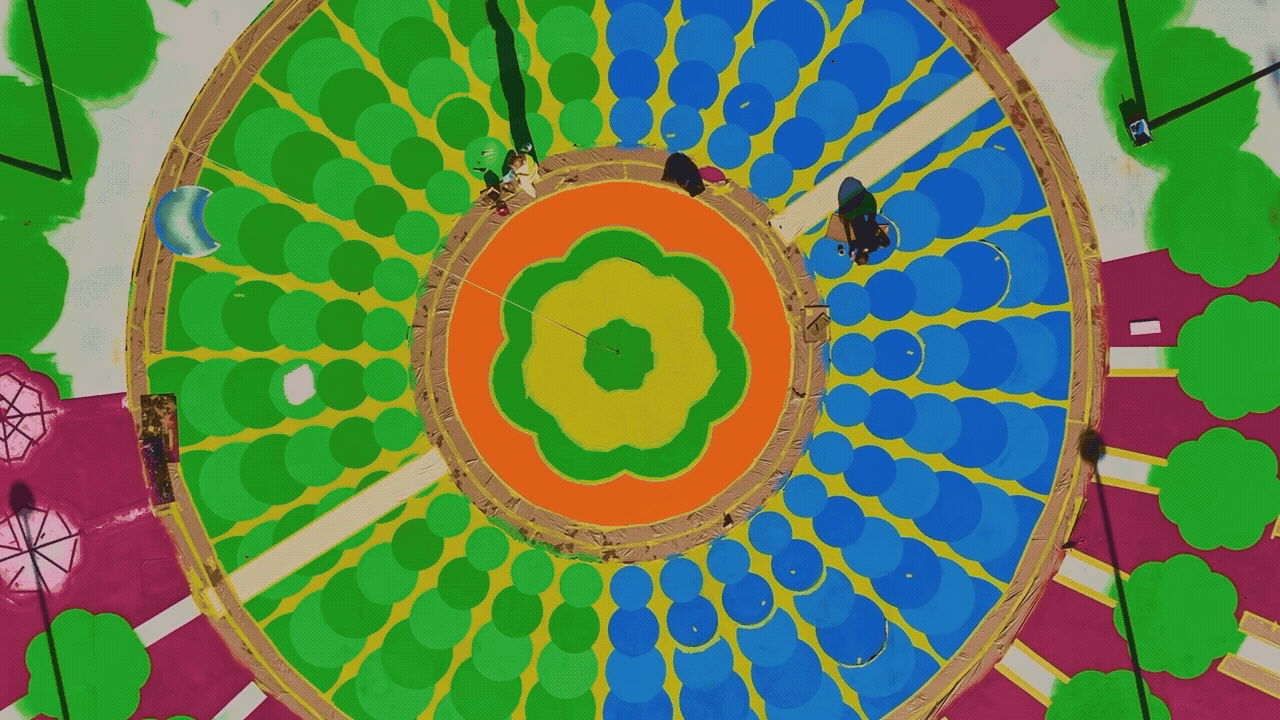 A drone shot of a huge, colorful geometric mural being painted on the ground.