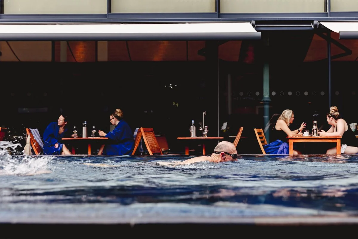 People dining at outdoor tables with a swimming pool in the foreground.