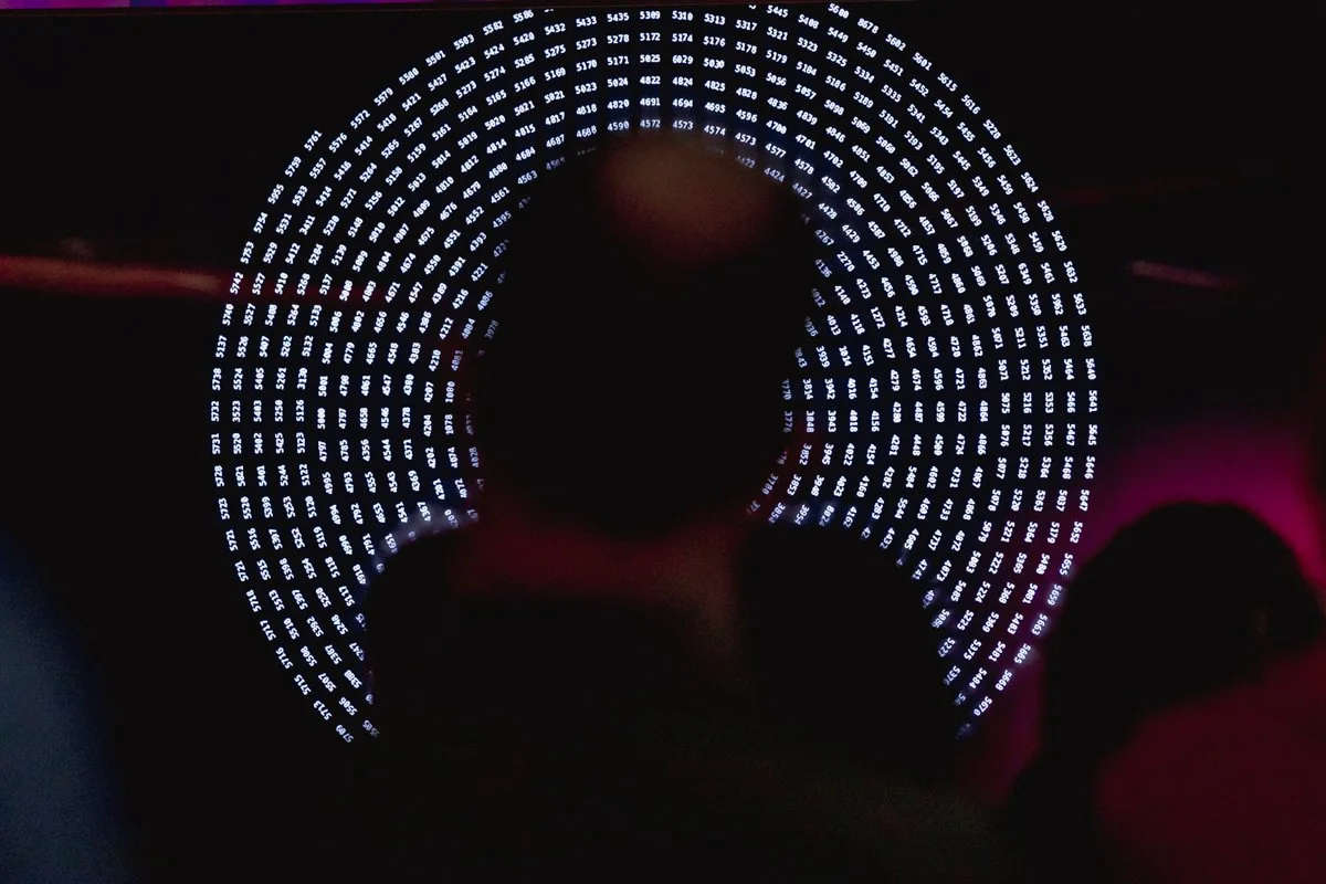 A person taking a photo of a circular display of numbers in white LED lights, which are arranged in concentric rings against a dark background.