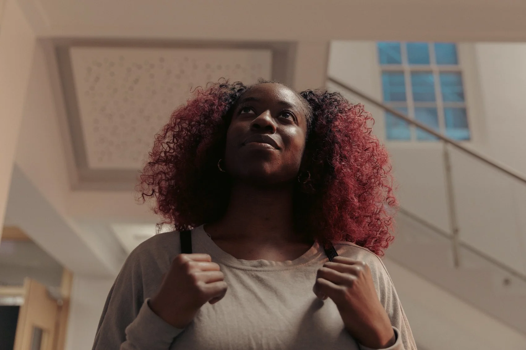 A woman with curly red and black hair carrying a backpack in an indoor setting