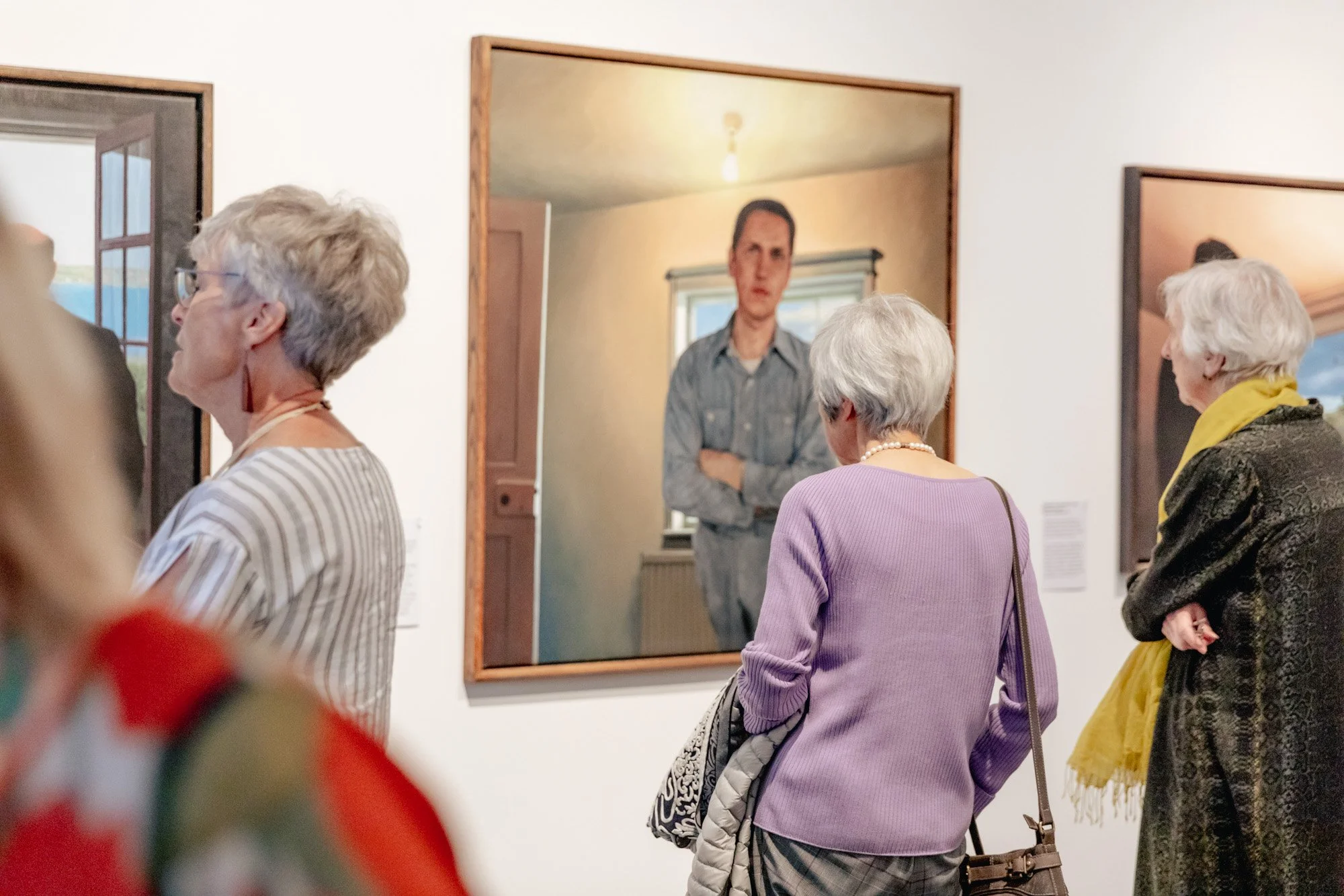 Gallery visitors observing artwork, including a woman in a purple sweater and pearl necklace facing a large Classical portrait of a man in a blue shirt.