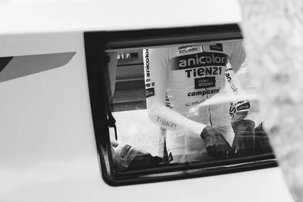 A cyclist's torso and arms reflected in a mirror or glass, with cycling gear and sponsorship logos visible.