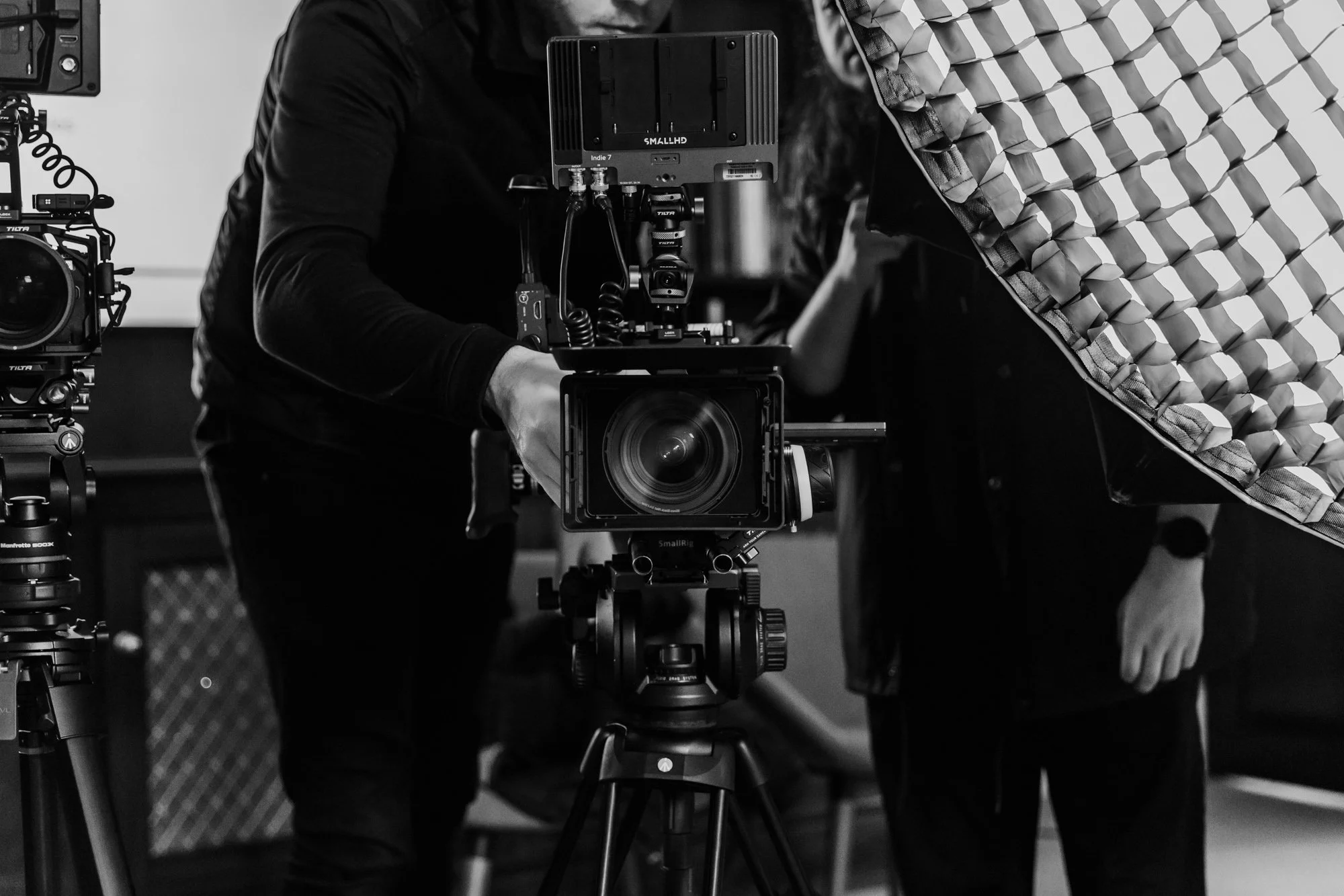 Filmmakers operating professional camera equipment in a studio, with lighting setup and other gear visible.