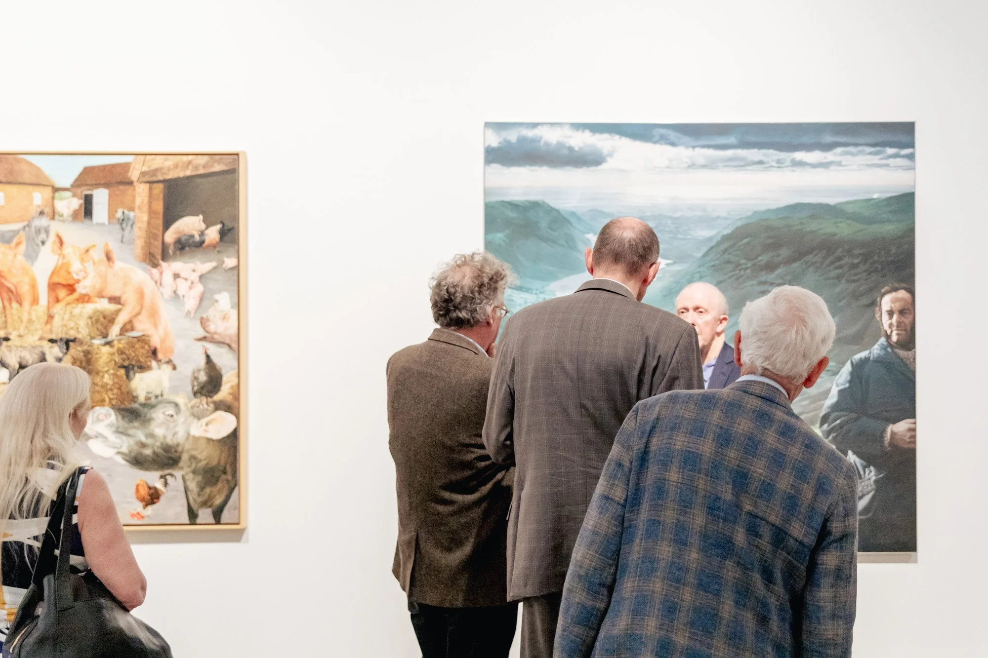 Group of six people viewing artwork in an art gallery, with a large landscape painting and a painting of animals on the wall.