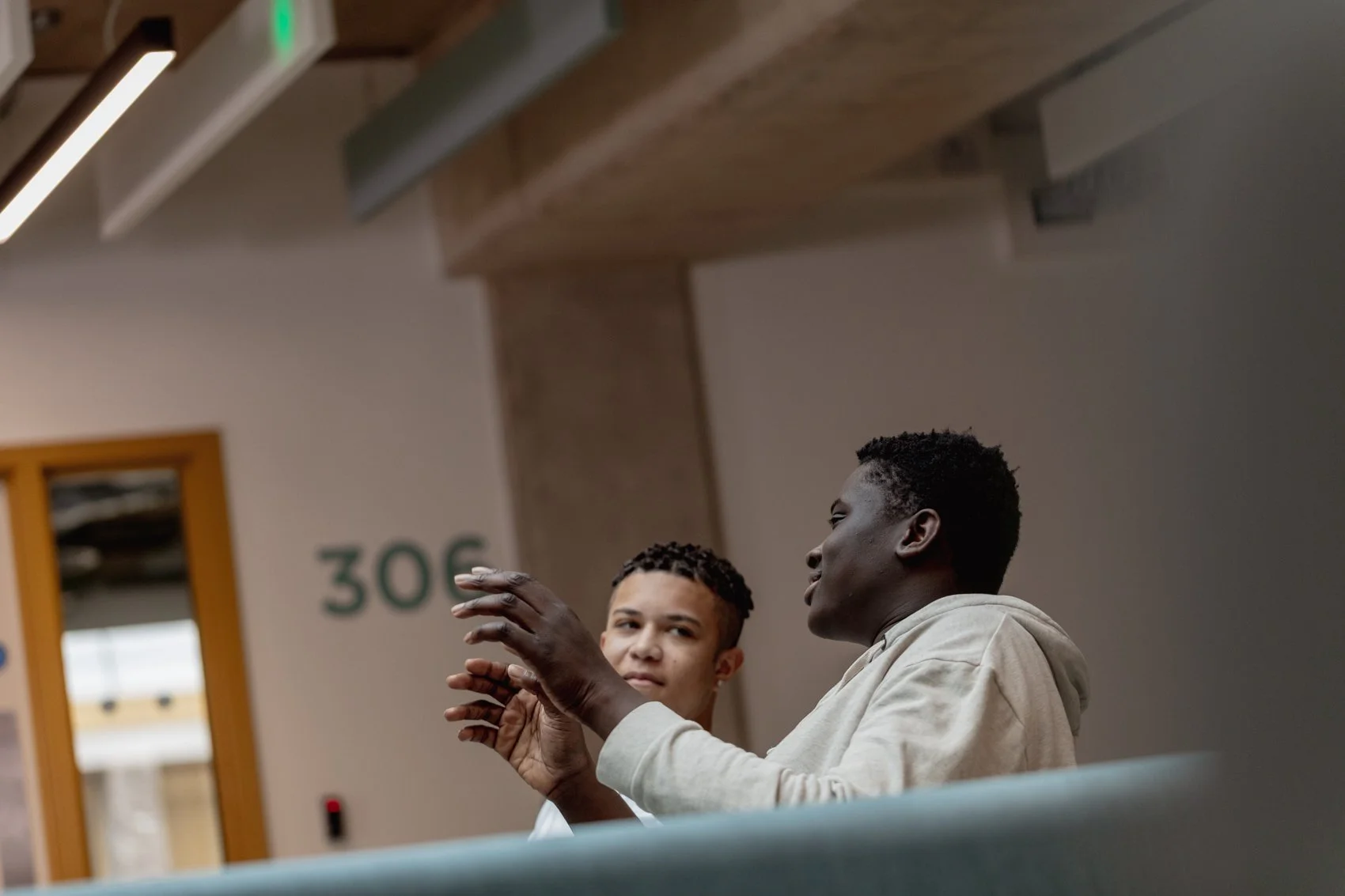 Two men sitting indoors, engaged in conversation, with one gesturing with his hands.
