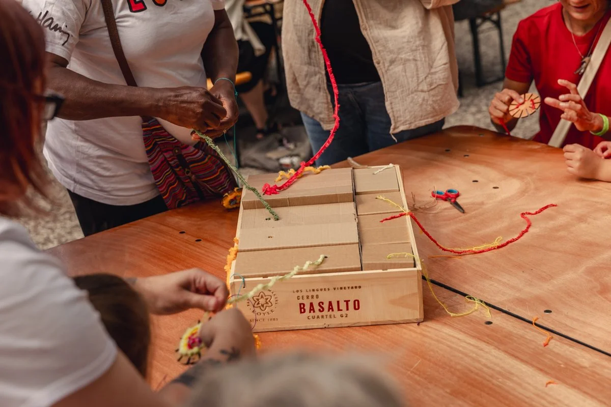 People making a craft with yarn and scissors around a wooden table.
