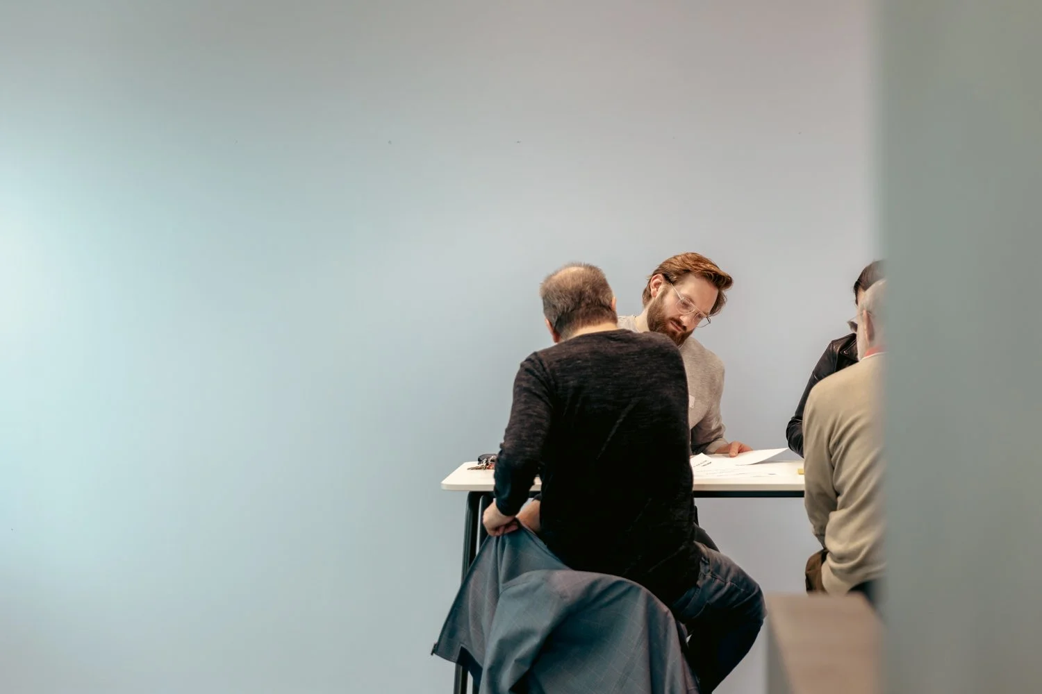 Four men sitting at a table engaged in conversation in a modern, minimalistic room.