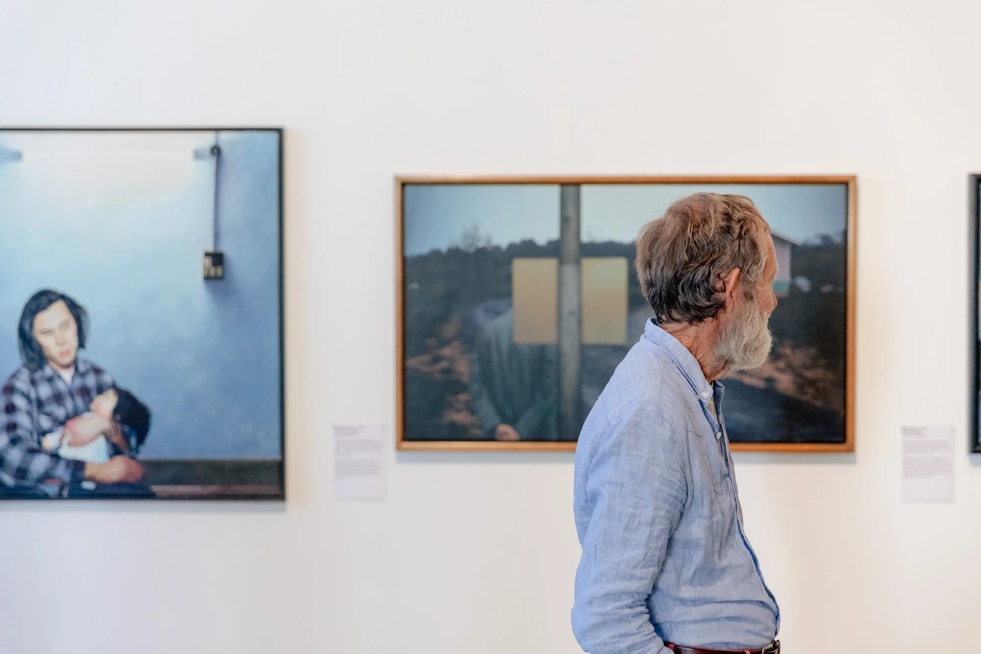 Older man with gray hair and beard looking at artwork in a gallery.