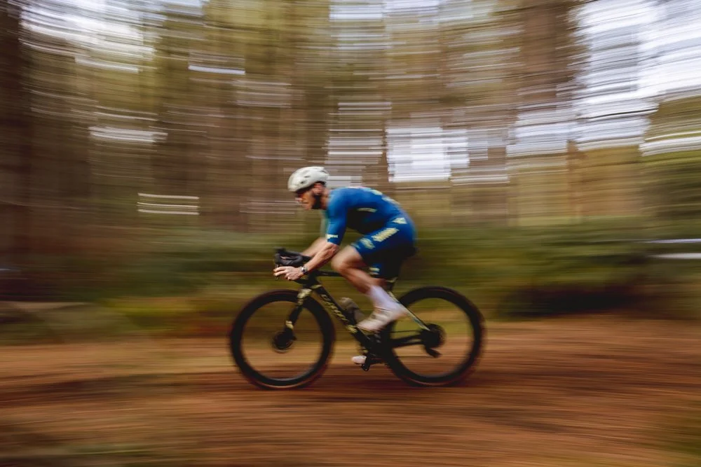 A person riding a mountain bike through a forest, with motion blur showing speed.