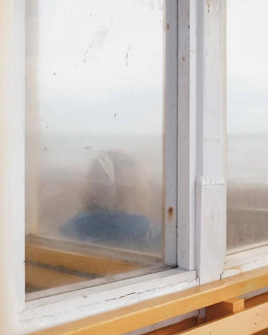 Close-up of a dirty, foggy window with a wooden windowsill, showing signs of wear and rust.