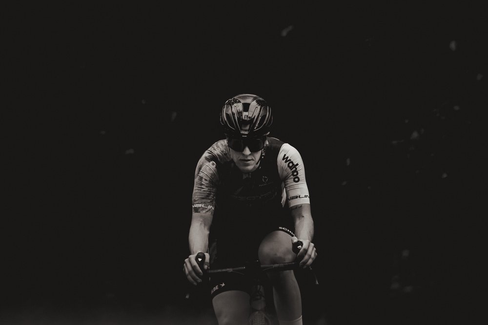 A cyclist wearing a helmet and sunglasses riding a bike in dark or low-light conditions.