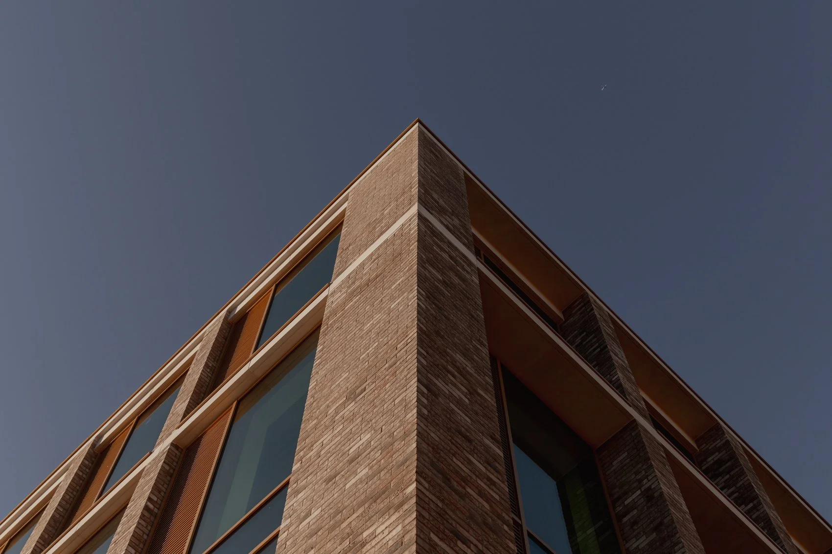 Low-angle view of a modern brick building with large windows against a clear blue sky.