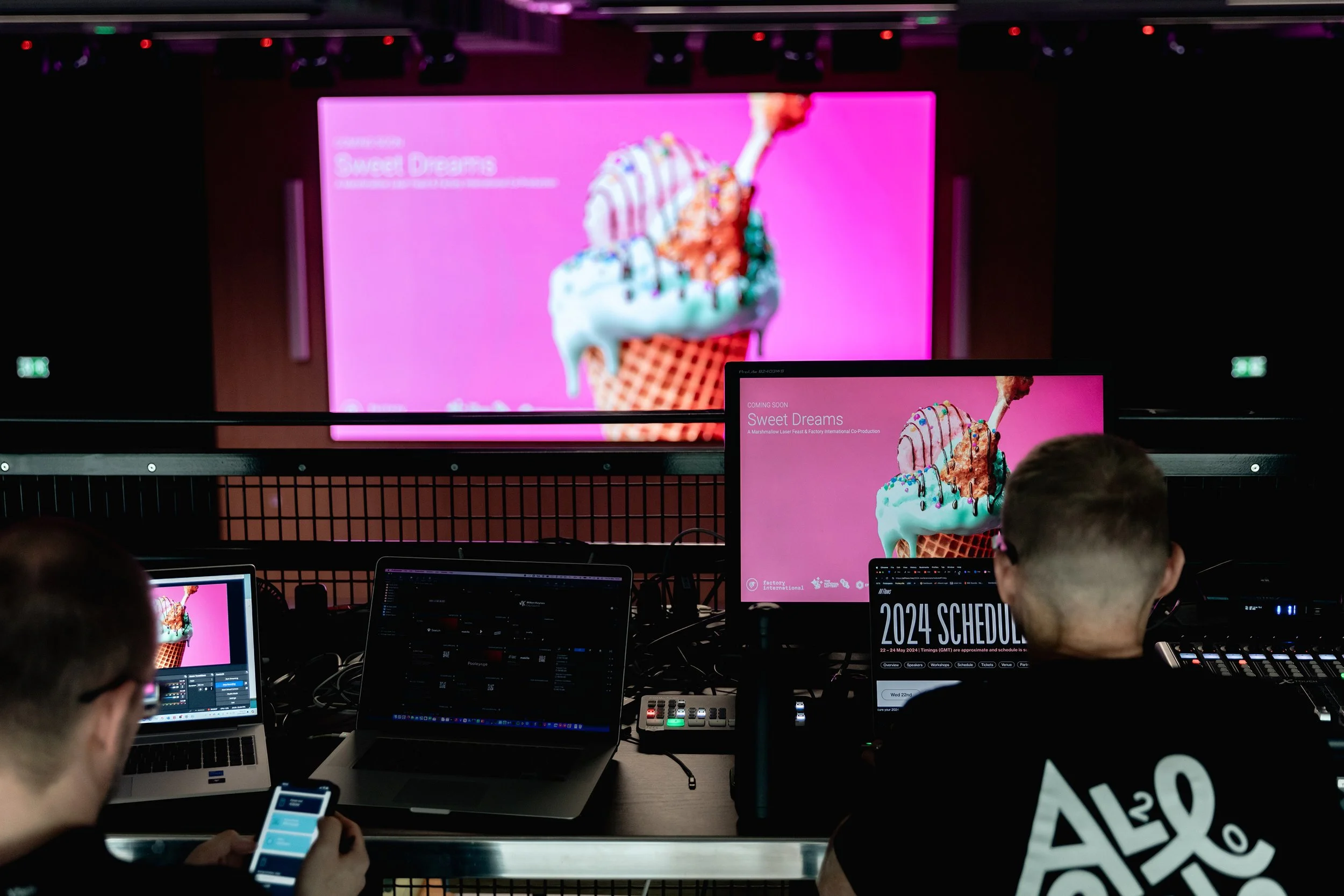 Control room with two operators in front of multiple monitors displaying promotional materials for an ice cream flavor called 'Sweet Dreams,' featuring a pink background with a close-up image of ice cream in a cone.