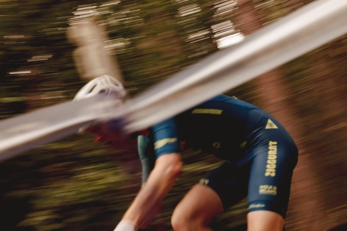 A cyclist wearing a helmet and blue cycling gear falling in a wooded area, with motion blur showing fast movement.