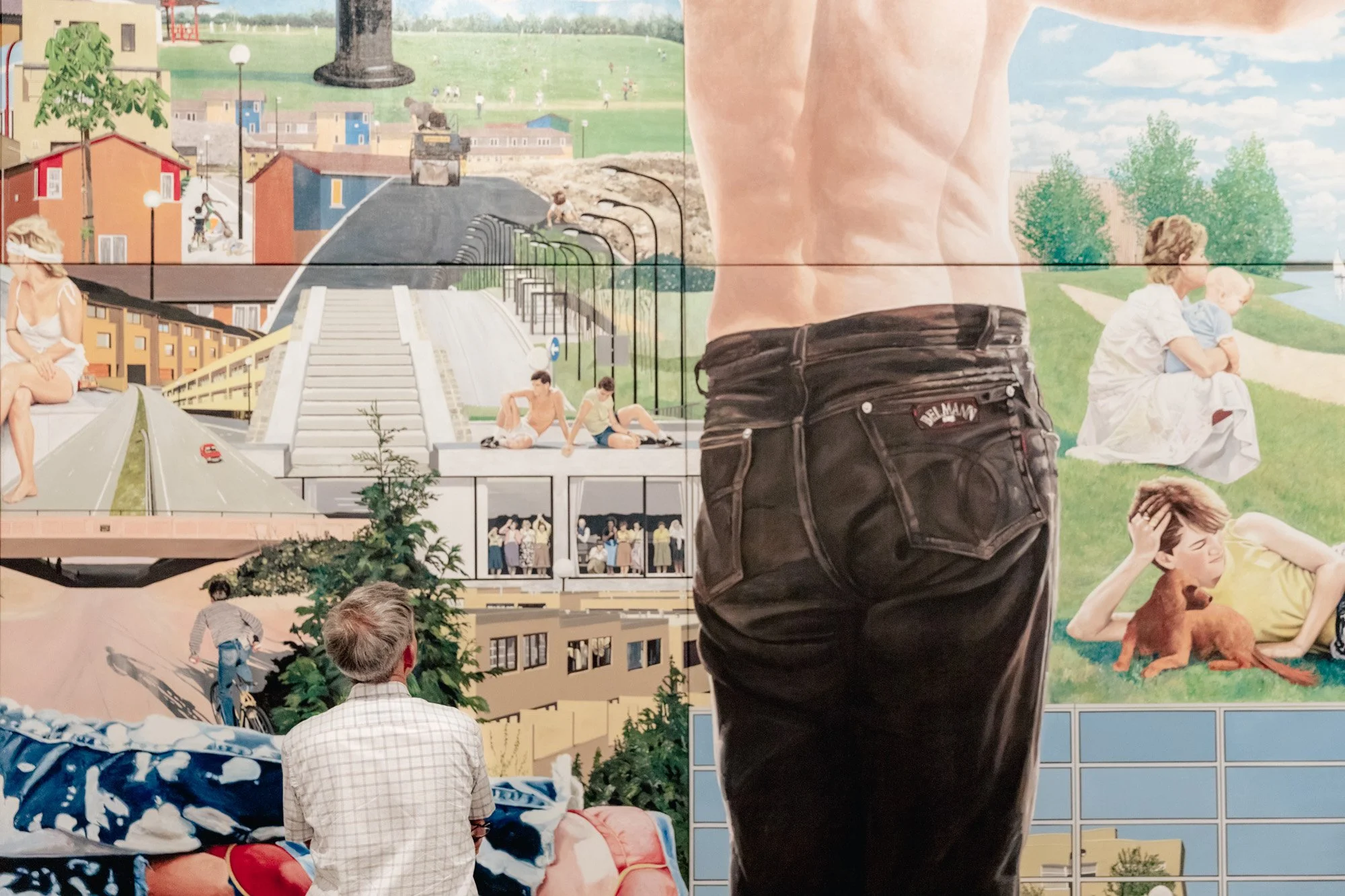 A large mural or collage depicting various scenes including people relaxing, children playing, a person riding a bike, and a cityscape with buildings, trees, and outdoor activities.