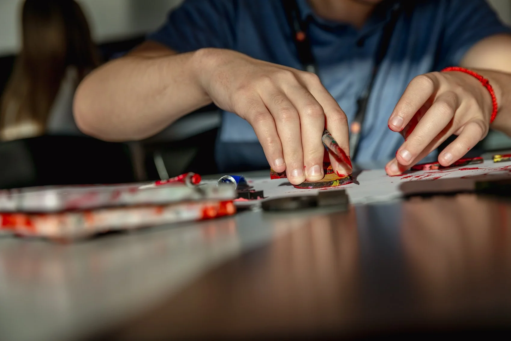 A person creating art with paint on a small canvas, using their fingers and a paintbrush, with art supplies scattered on the table.