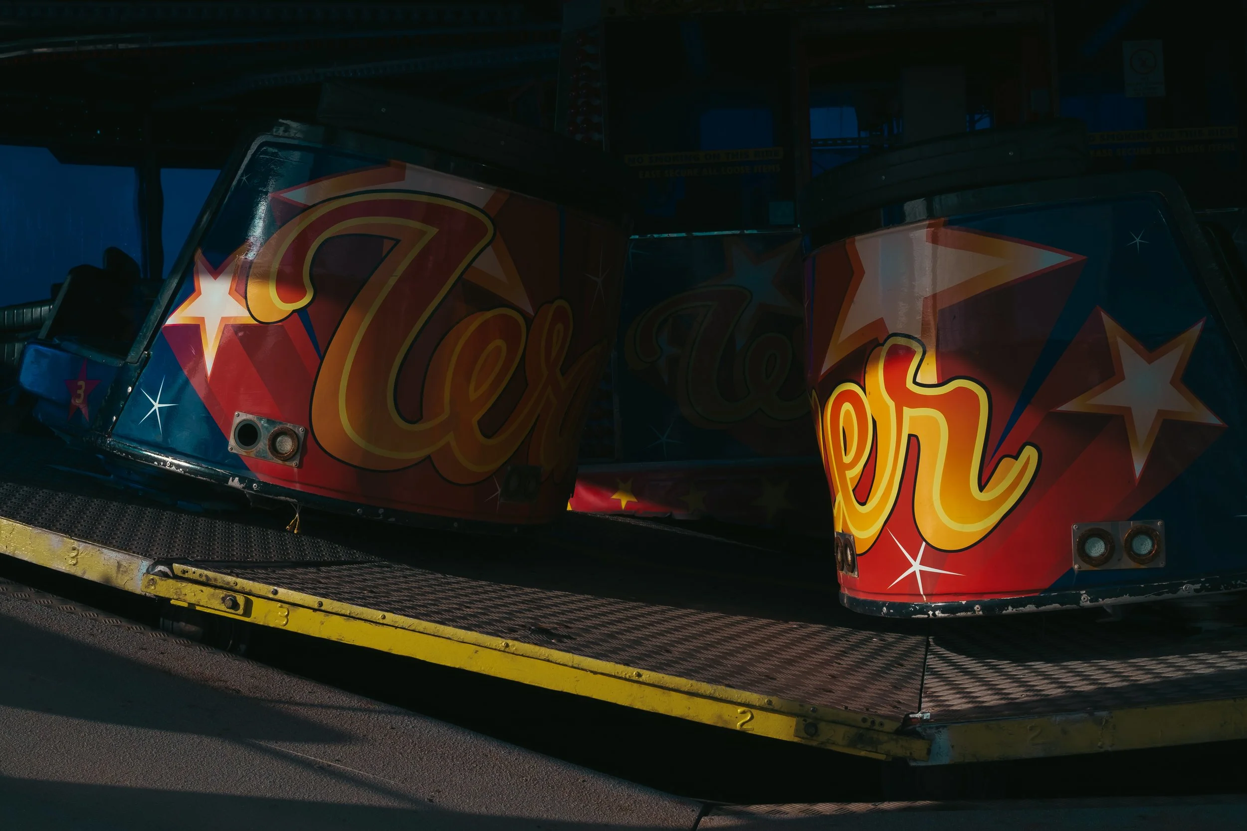 Colorful amusement park ride with the word 'Ler' on the front in large yellow and orange letters, decorated with stars and geometric patterns. It is positioned on a metal platform.