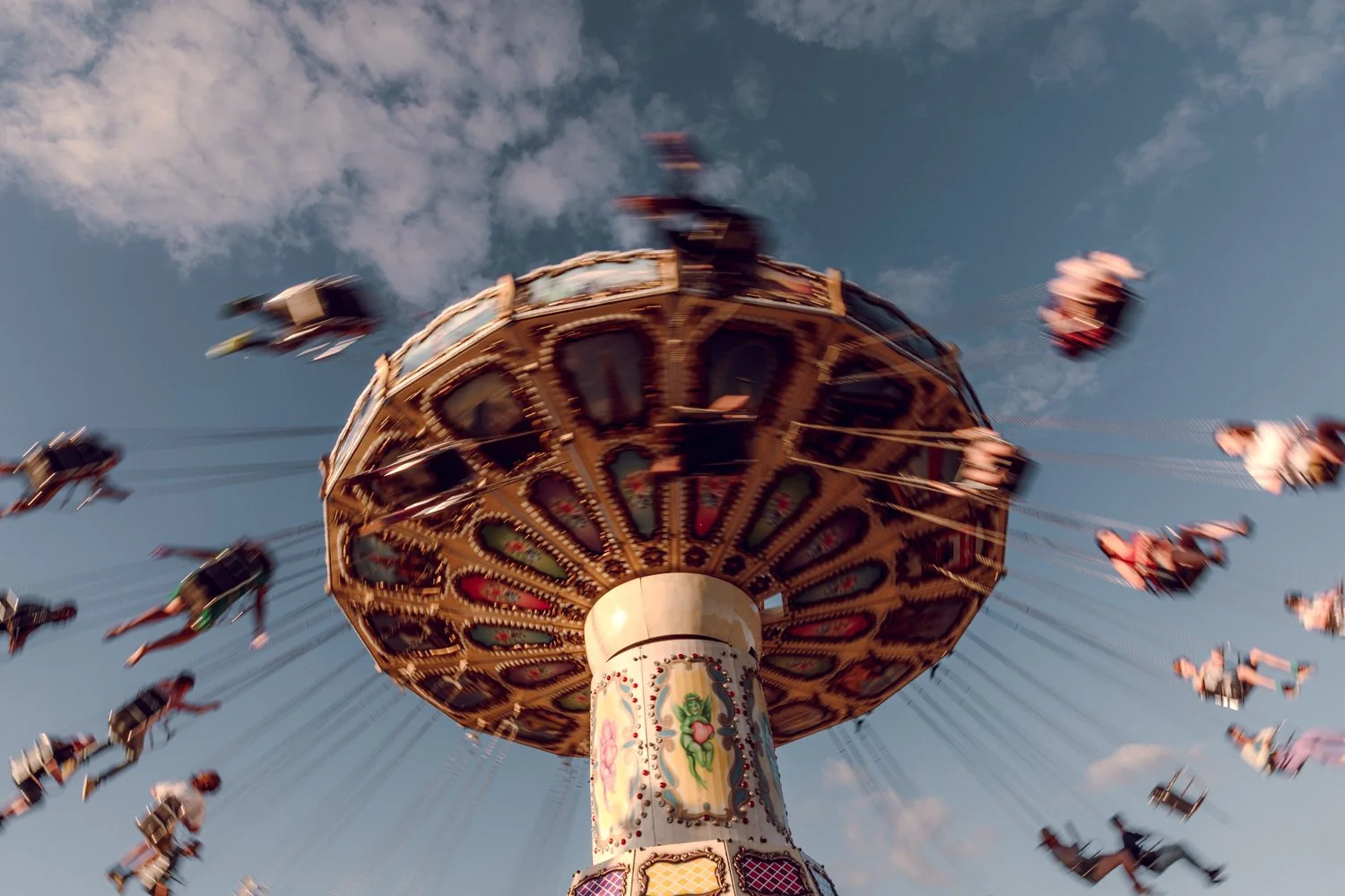 Colorful swing ride at an amusement park with people swinging around in the sky against a blue sky with clouds.