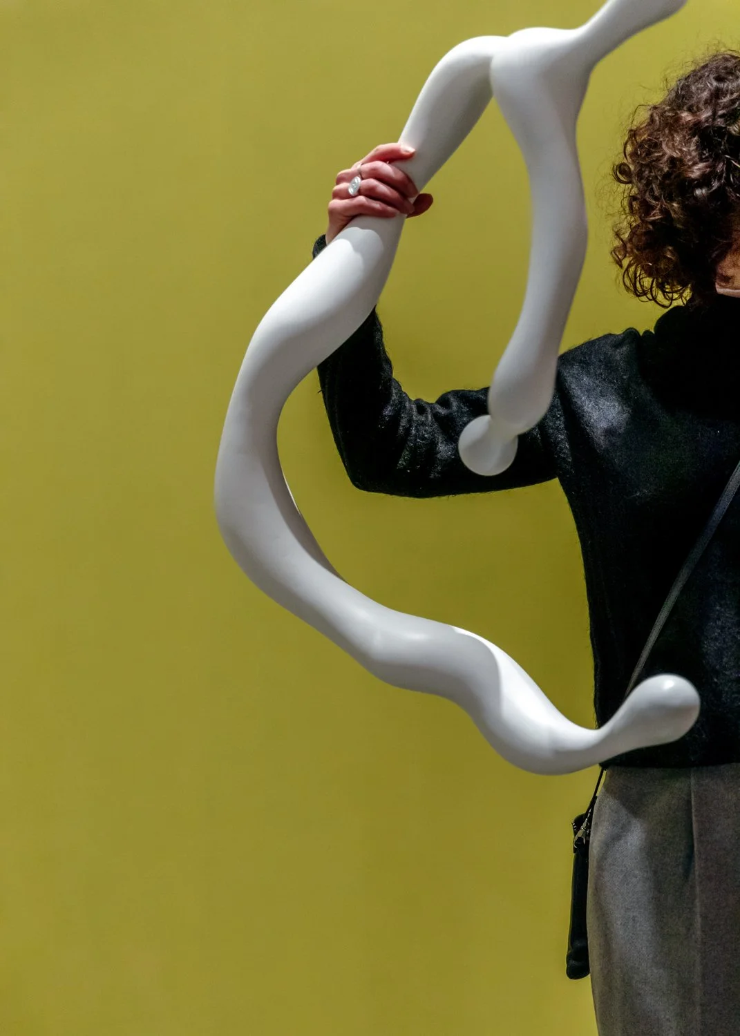 Close-up of a person holding a large, white, abstract sculpture with a curvy, knot-like shape, against a yellow background.