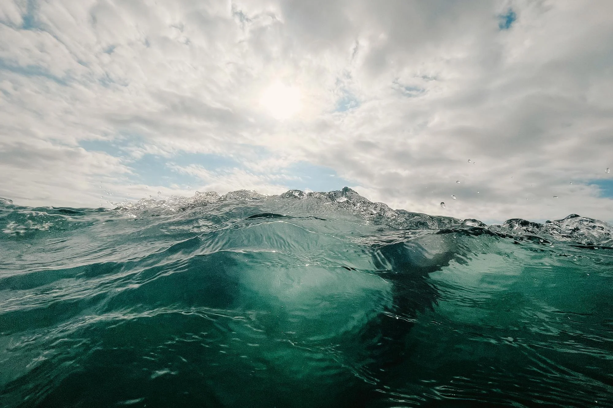 Open ocean water with small waves, partly cloudy sky with the sun visible.