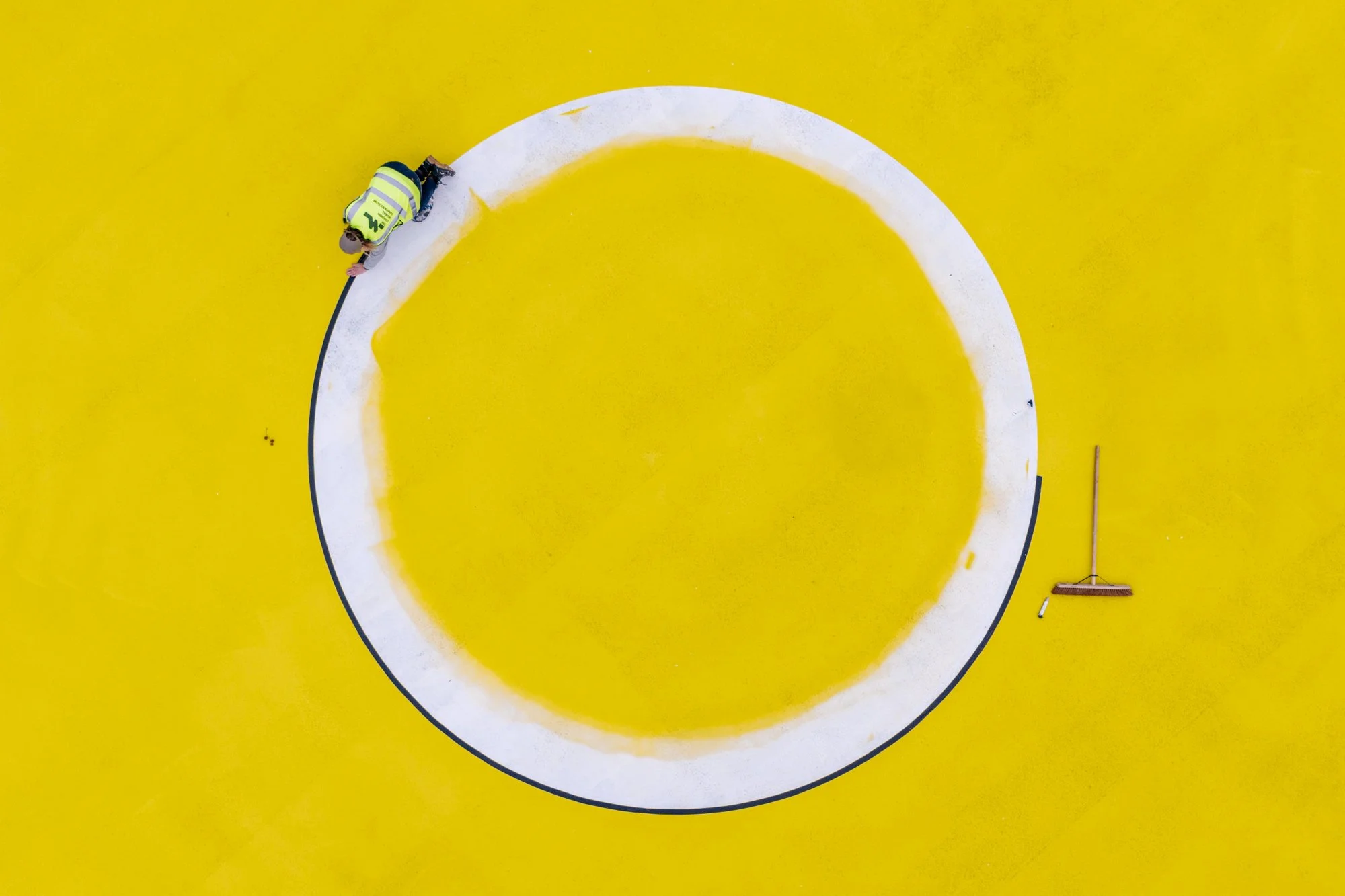 A worker painting a large white circle on a bright yellow floor.