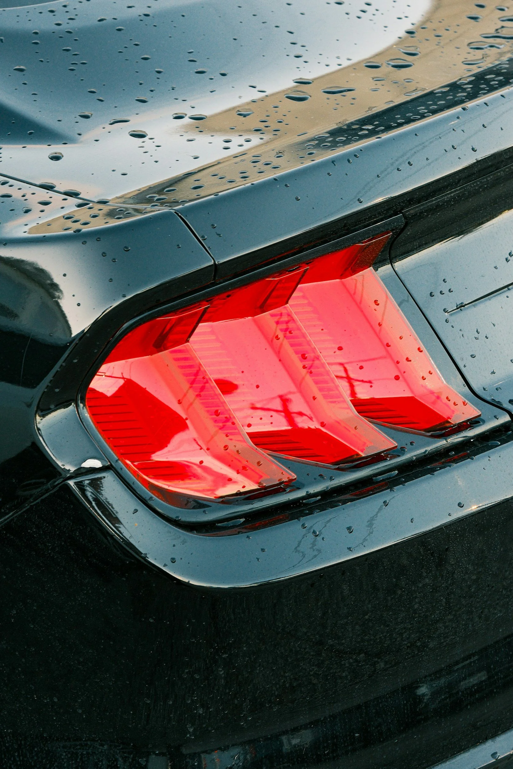 Close-up of the rear tail light of a black car with water droplets on the surface.