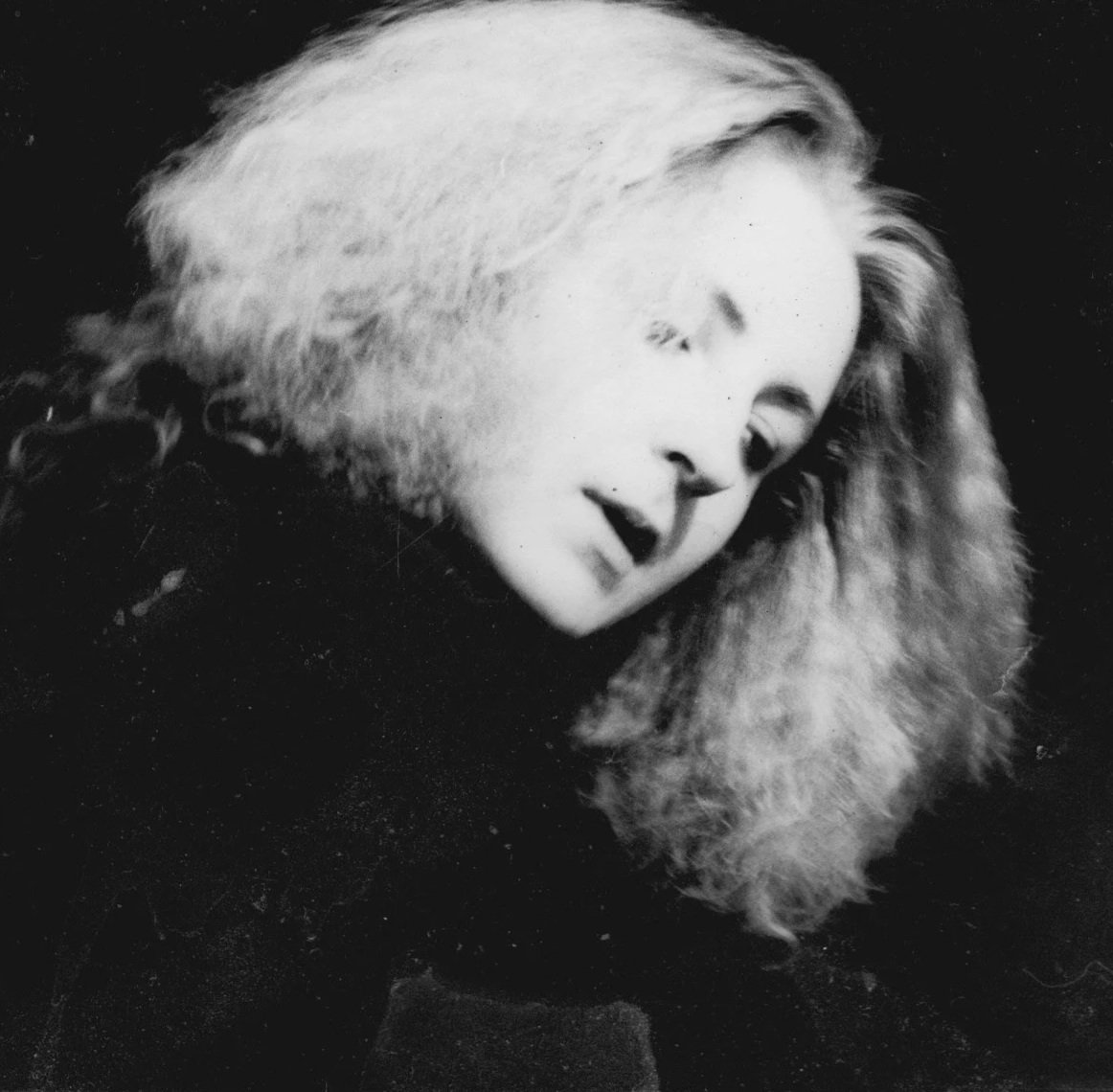 Black and white photograph of a woman with light-colored hair wearing a fur garment or collar, with her eyes closed and head slightly tilted.