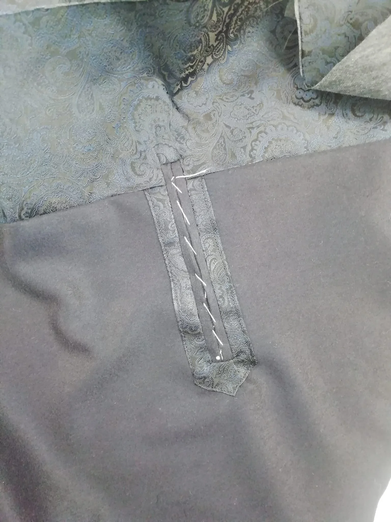 Close-up of a hand-crafted jetted internal pocket on a bespoke men's jacket, featuring a paisley silk lining and secured with temporary basted cross-stitching during the assembly process in the Elena Milani studio.