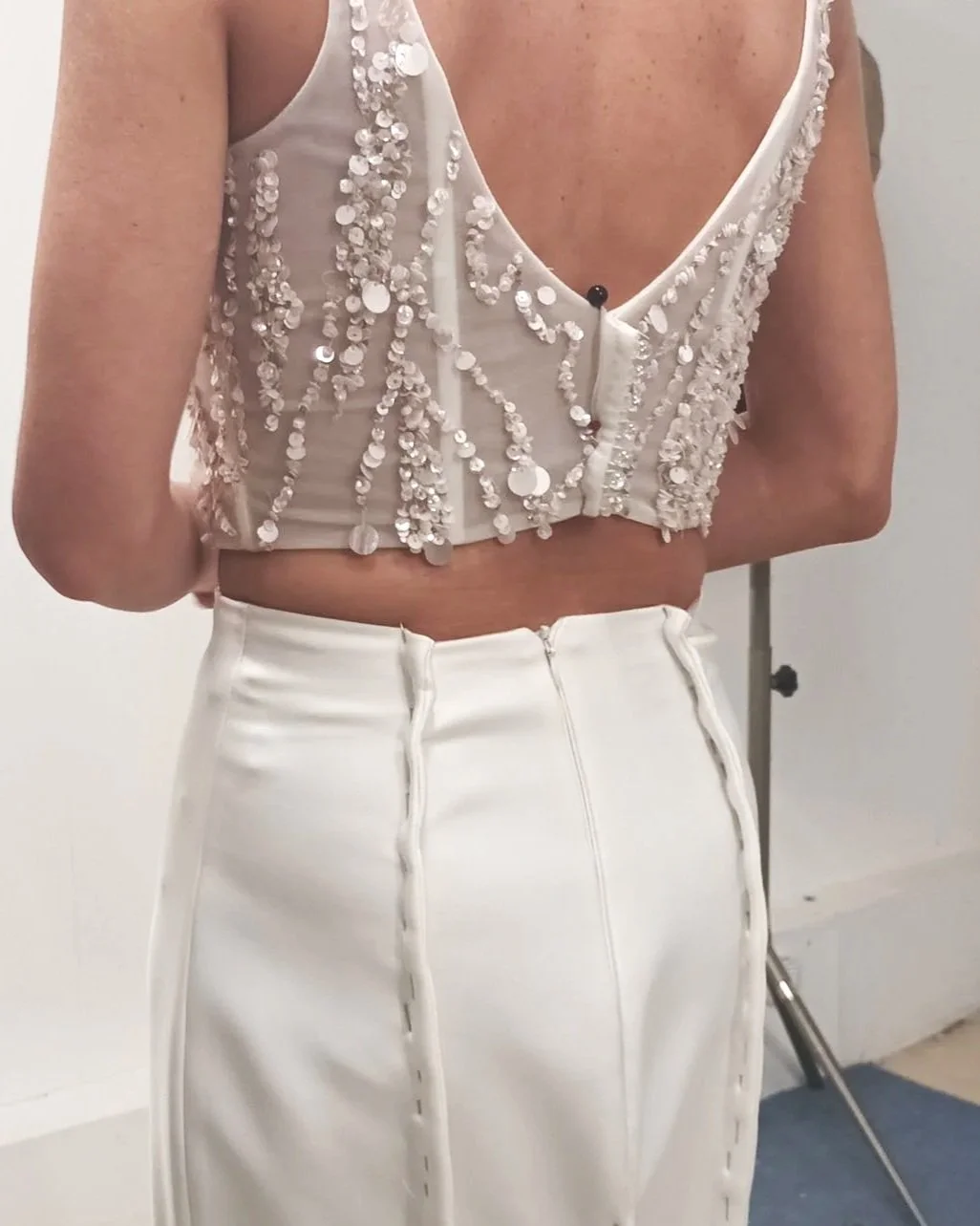 A woman wearing a white halter top with sequins and a zipper, and a high-waisted white skirt.