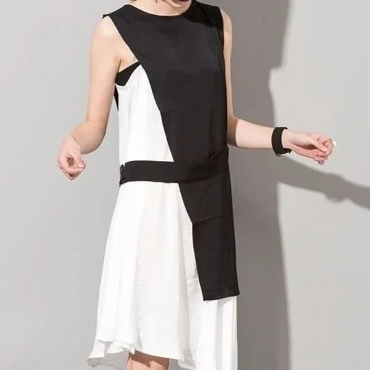 A person wearing a sleeveless black and white dress with a black waistband and a layered white skirt, standing against a gray background.