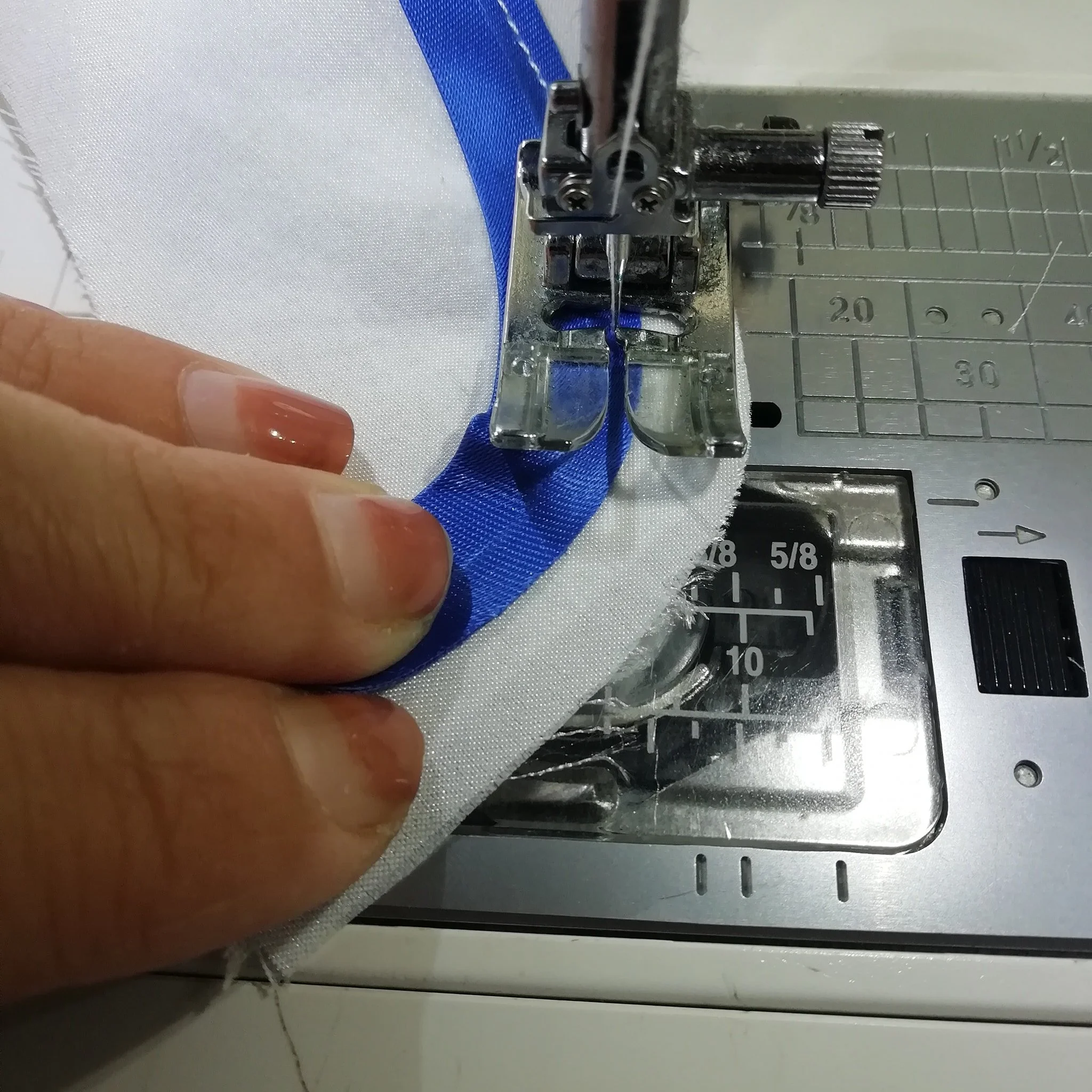 Close-up of sewing machine stitching a blue and white fabric together, with a person's fingers guiding the fabric.