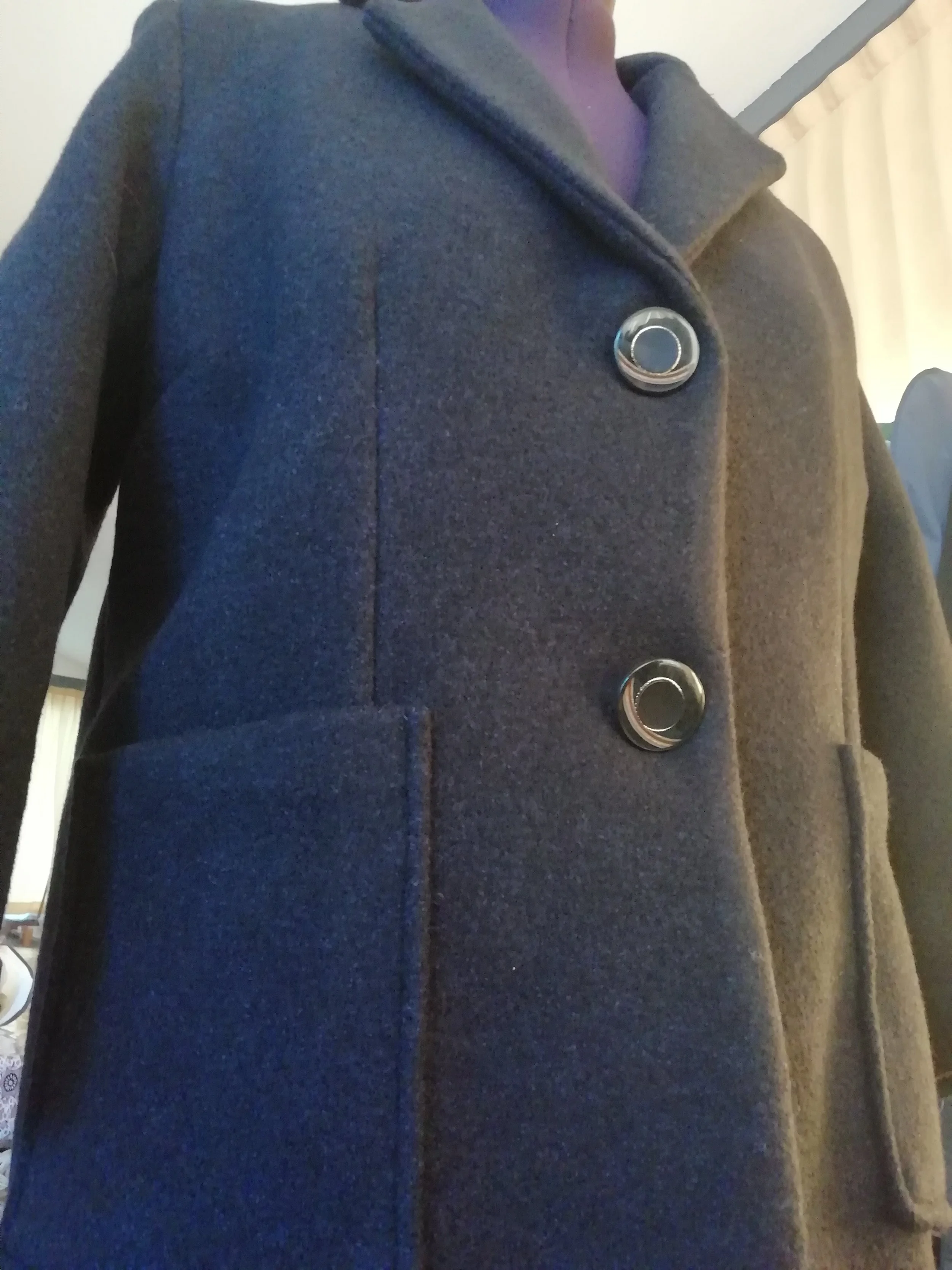 Close-up of a dark gray, button-up coat with large black buttons and a collar, worn by a person.