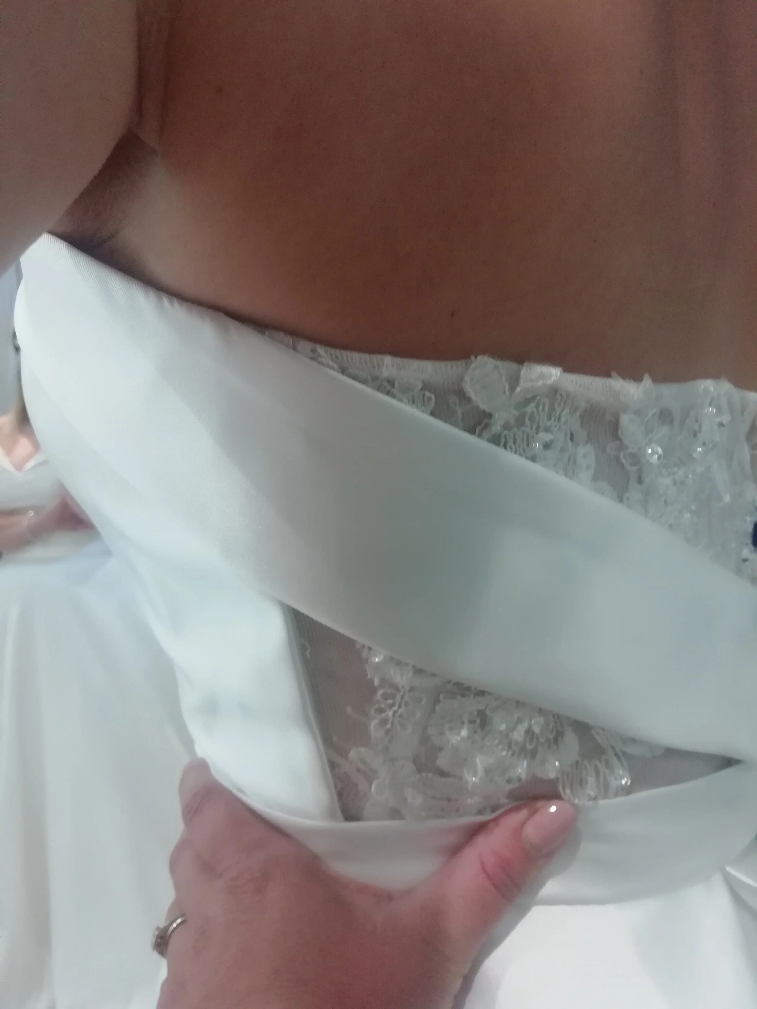 Close-up of a person holding a white satin wedding dress with lace and bead embellishments.