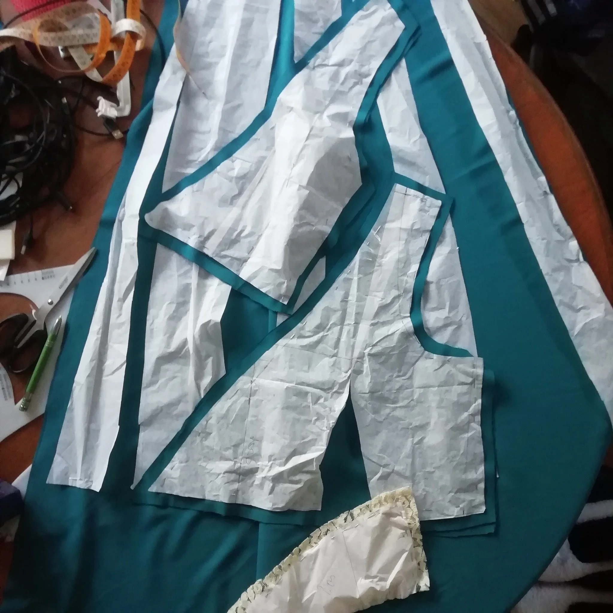 Hand-cut petrol green fabric pieces precisely shaped to bespoke patterns in my Burnham-on-Crouch studio, demonstrating the transition from mathematical drafting to garment assembly.