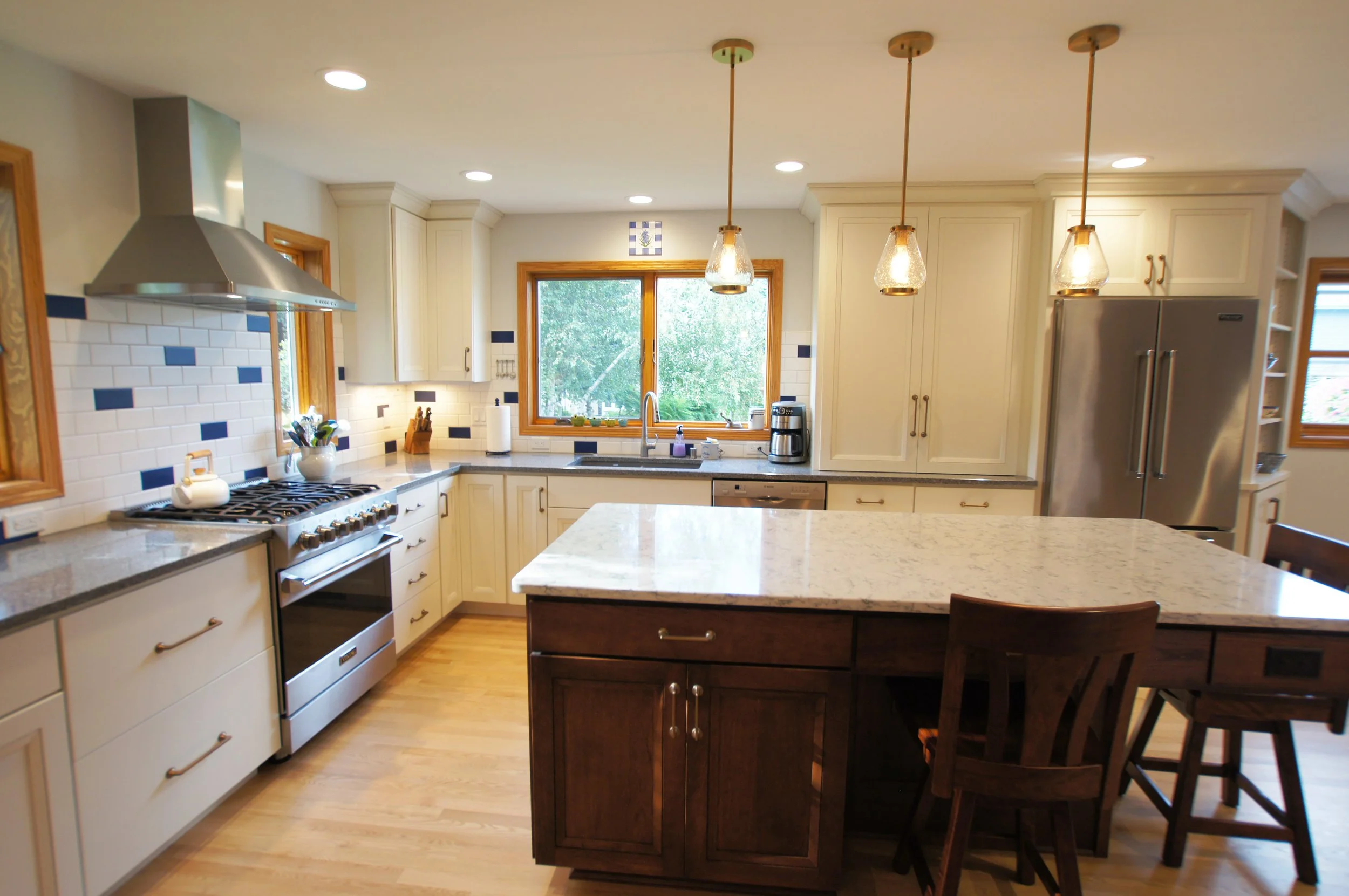 Bright kitchen with white cabinets, a large island with a granite countertop, stainless steel appliances, pendant lighting, and hardwood floors.