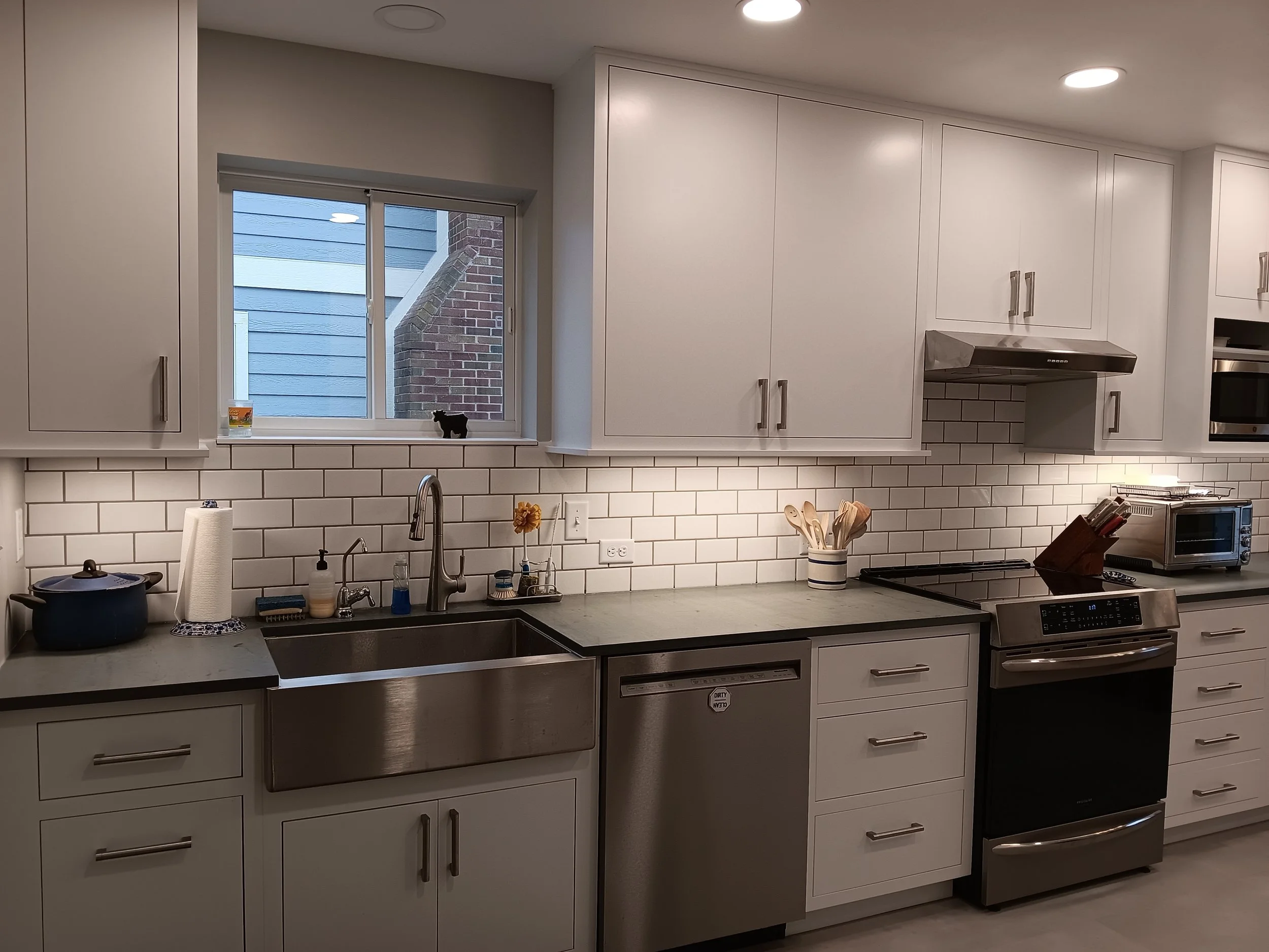 Modern kitchen with white cabinets, stainless steel appliances, a window above the sink, white subway tile backsplash, and various kitchen utensils and appliances on the countertop.
