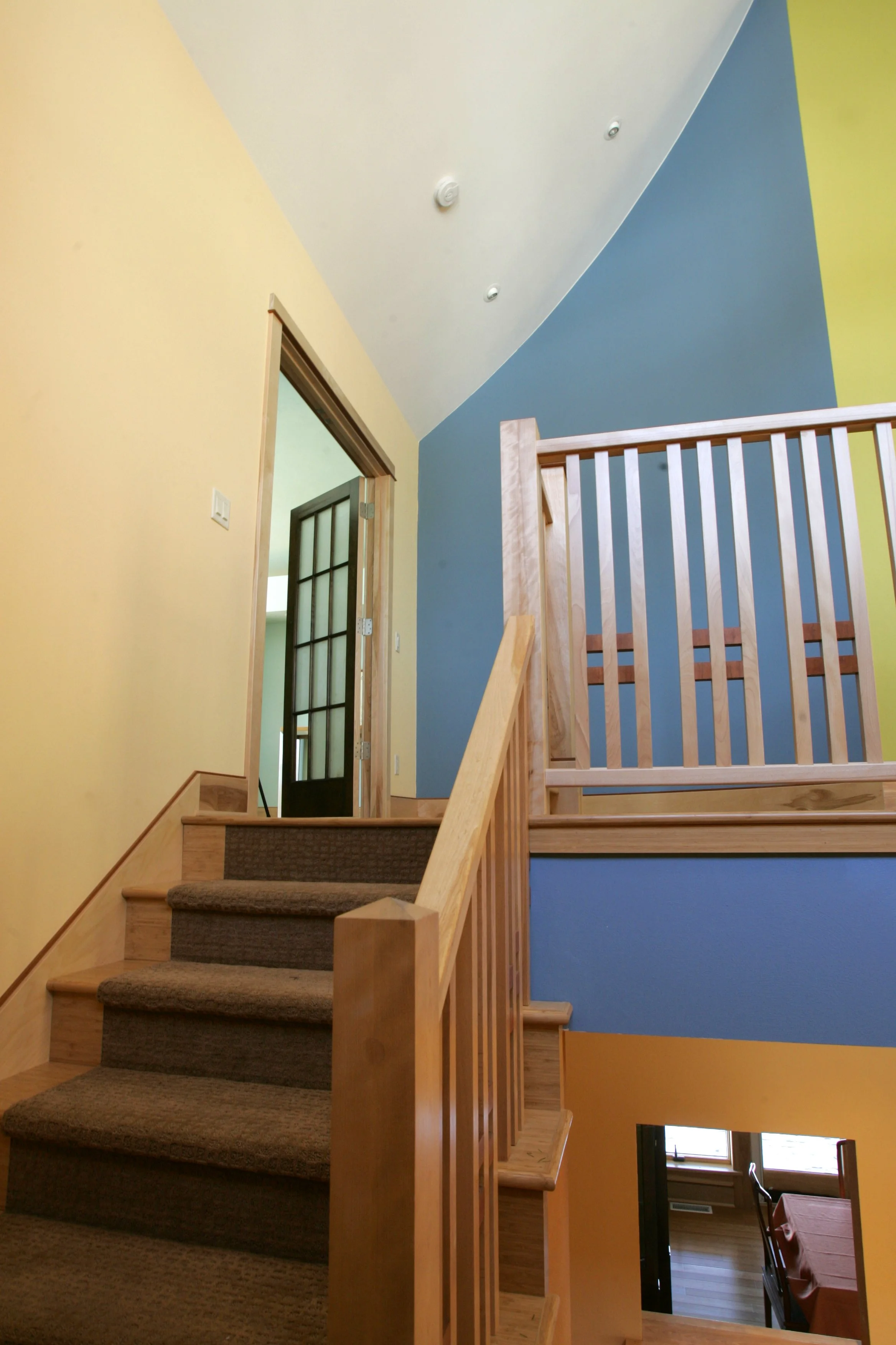 Interior view of a multilevel staircase area with colorful walls, a door with glass panels, and part of a dining area visible below.