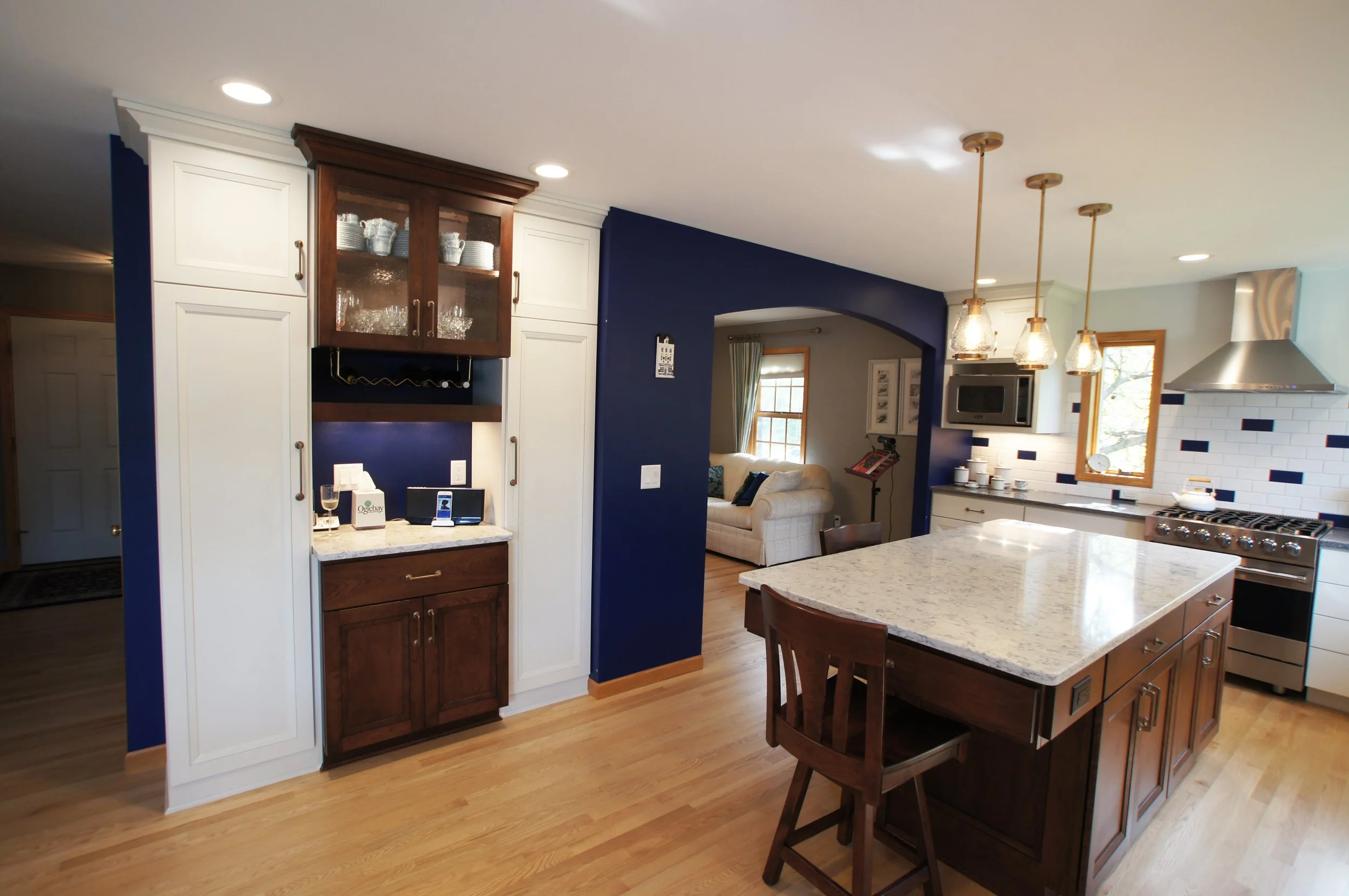 Modern kitchen with white cabinets, a central island with a granite top, blue accent wall, stainless steel stove, and hanging pendant lights.