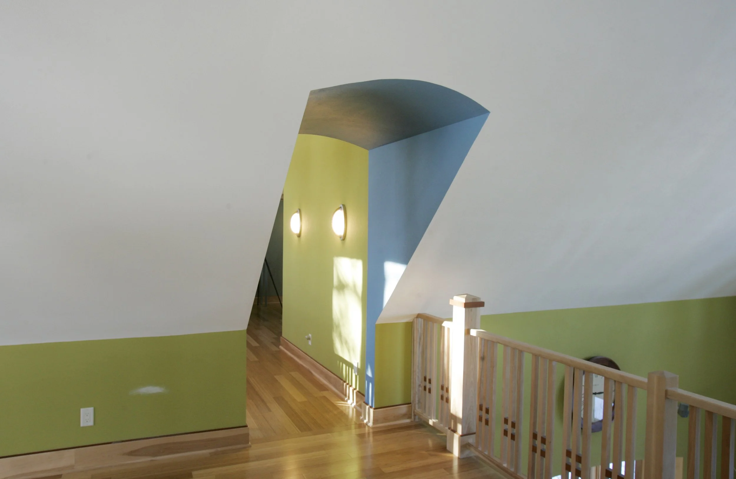 Interior view of a home with a sloped ceiling, green and white walls, hardwood floors, and a wooden railing.