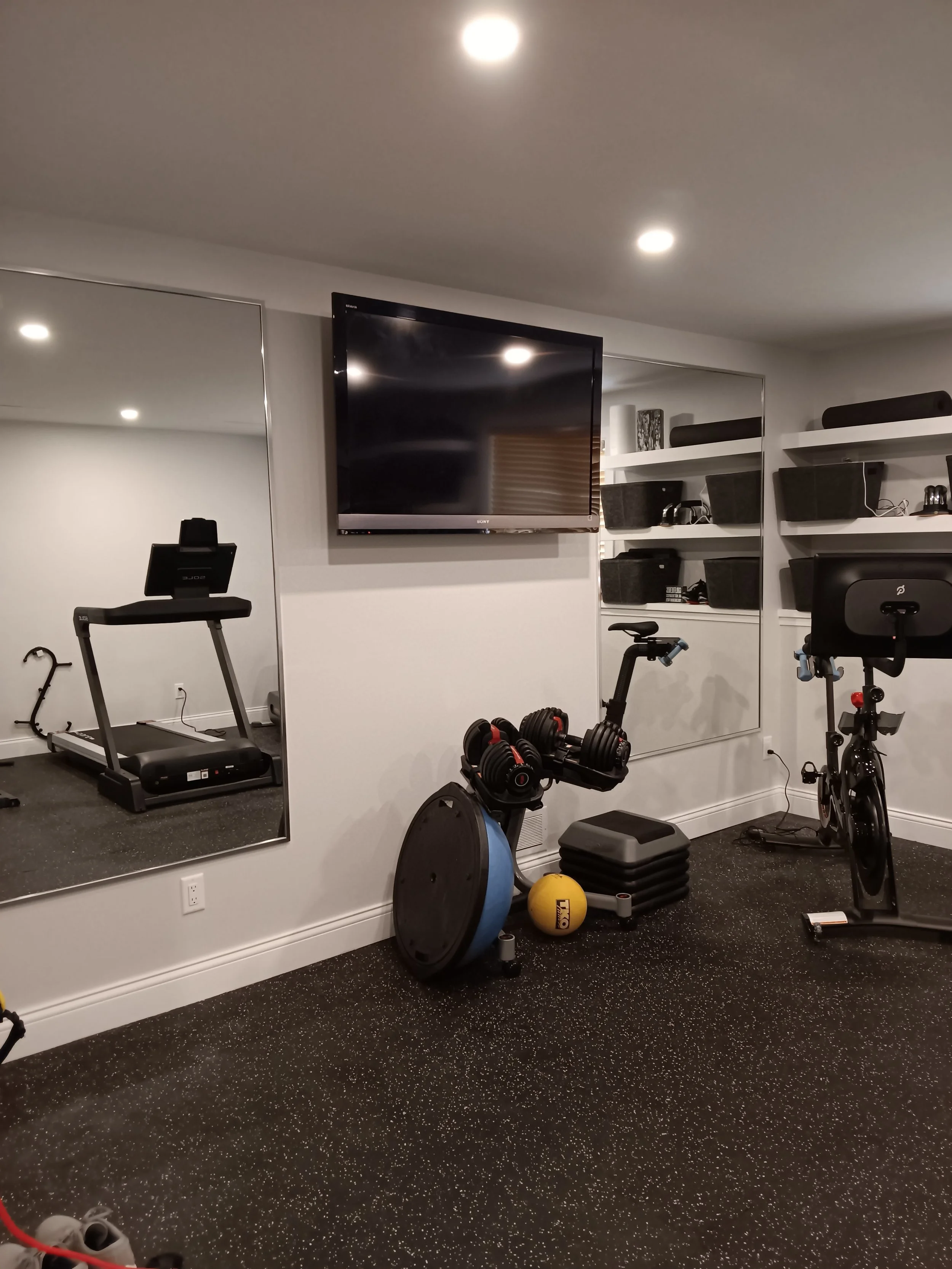 Home gym with treadmill, exercise bike, weight equipment, a large flat-screen TV, and mirrors on the wall.