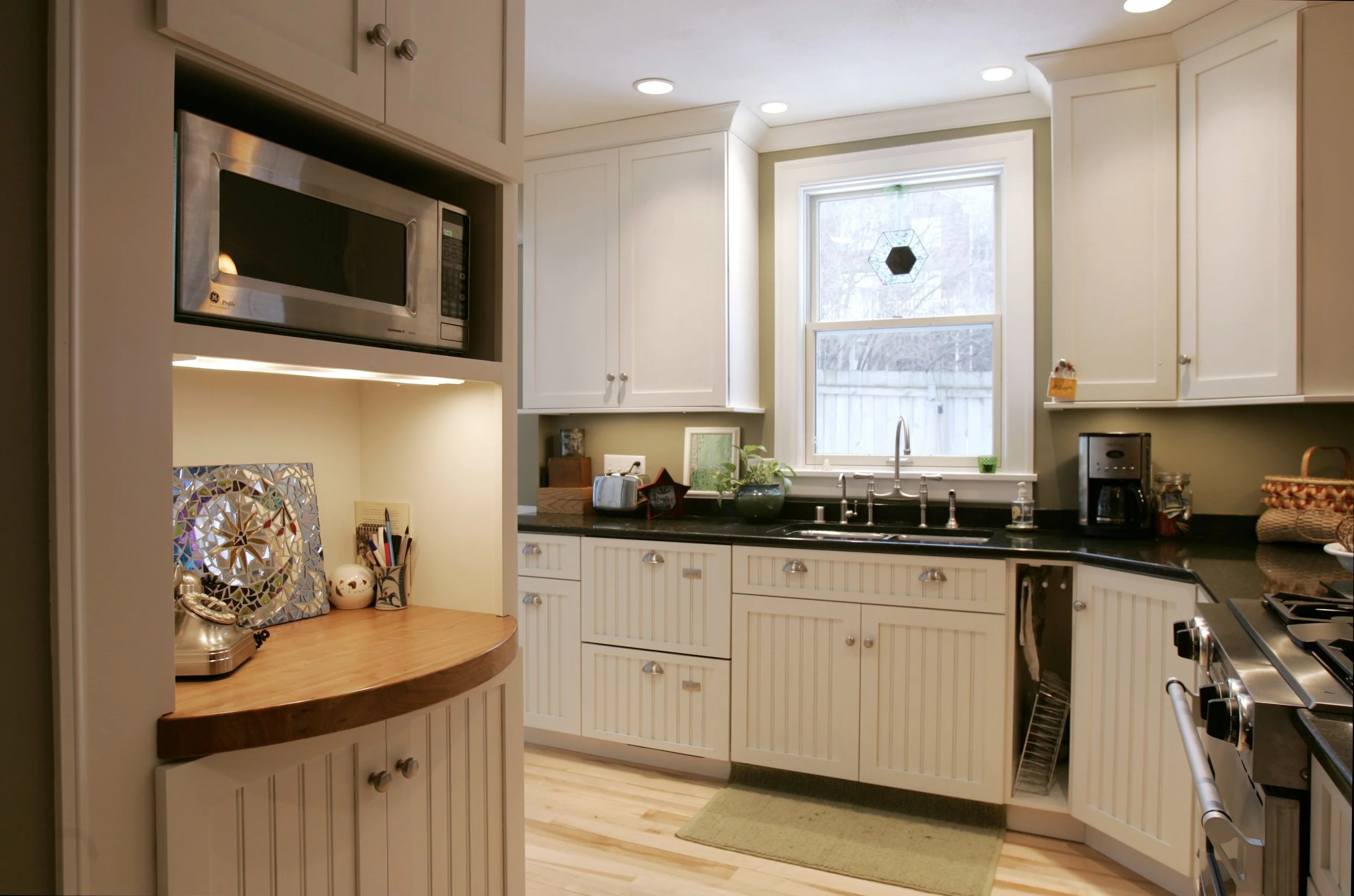 Kitchen with white cabinets, black countertop, window above sink, microwave, coffee maker, and decorative items.