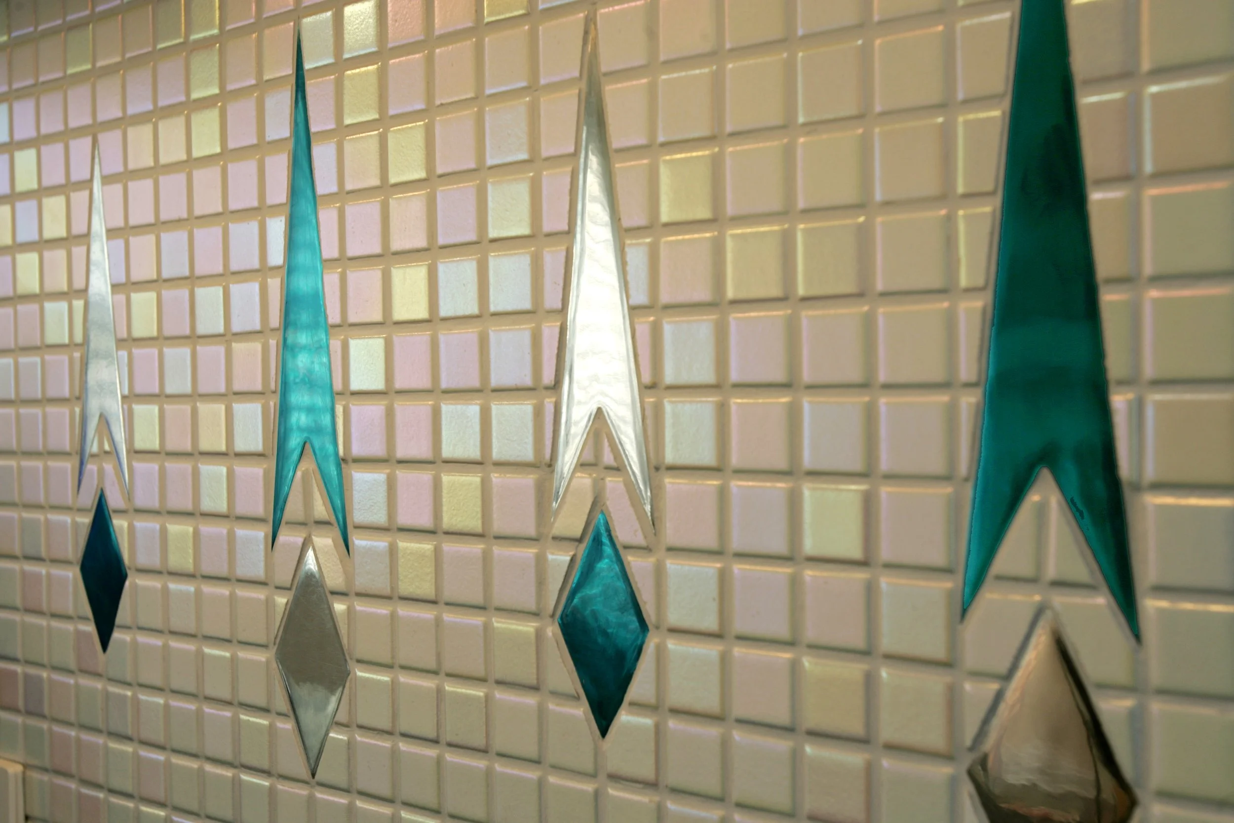 Decorative wall with glass star and diamond shapes in turquoise and silver, mounted on a white tile background.