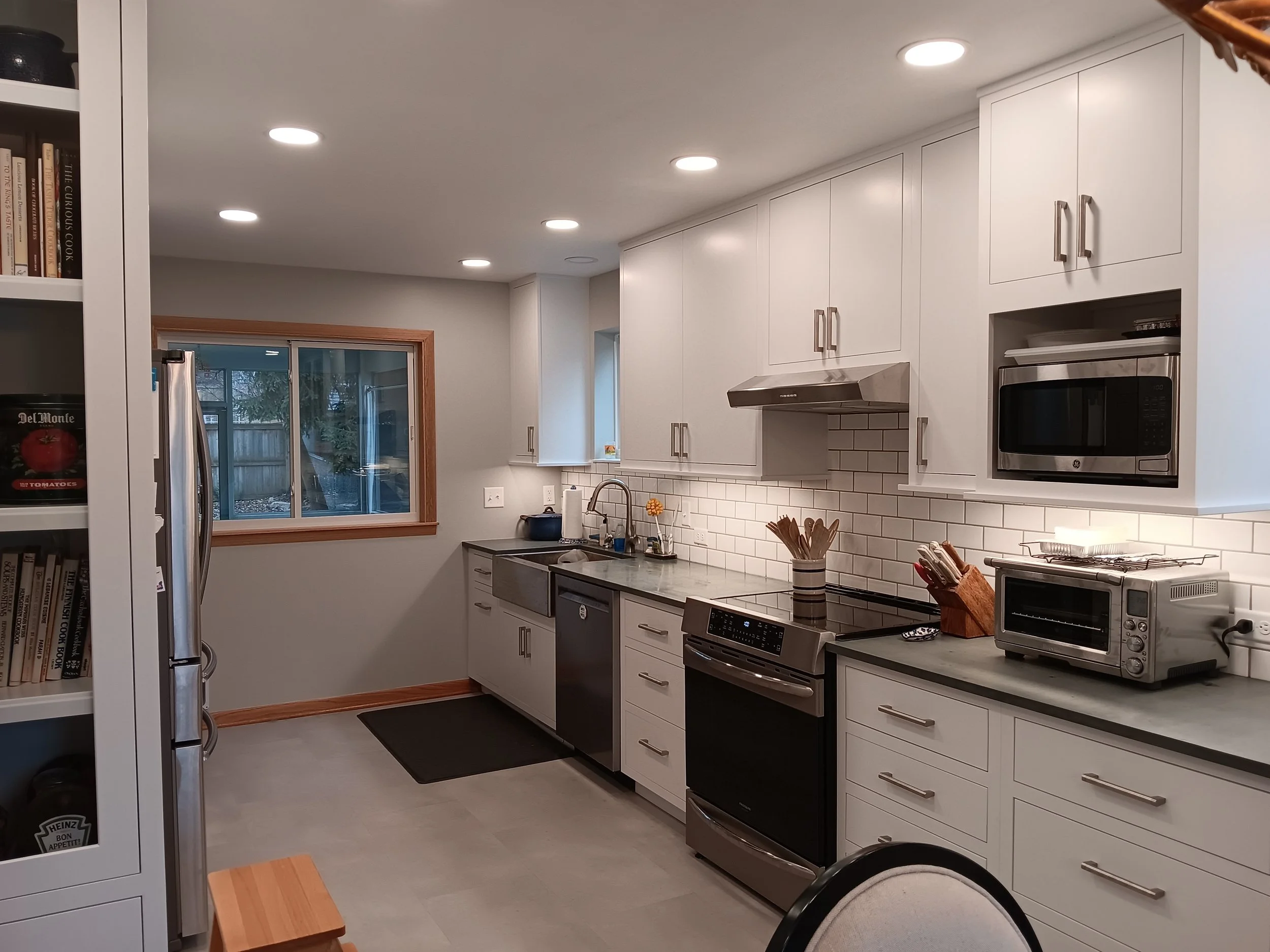 Modern kitchen with white cabinets, stainless steel appliances, a window, and recessed ceiling lights.