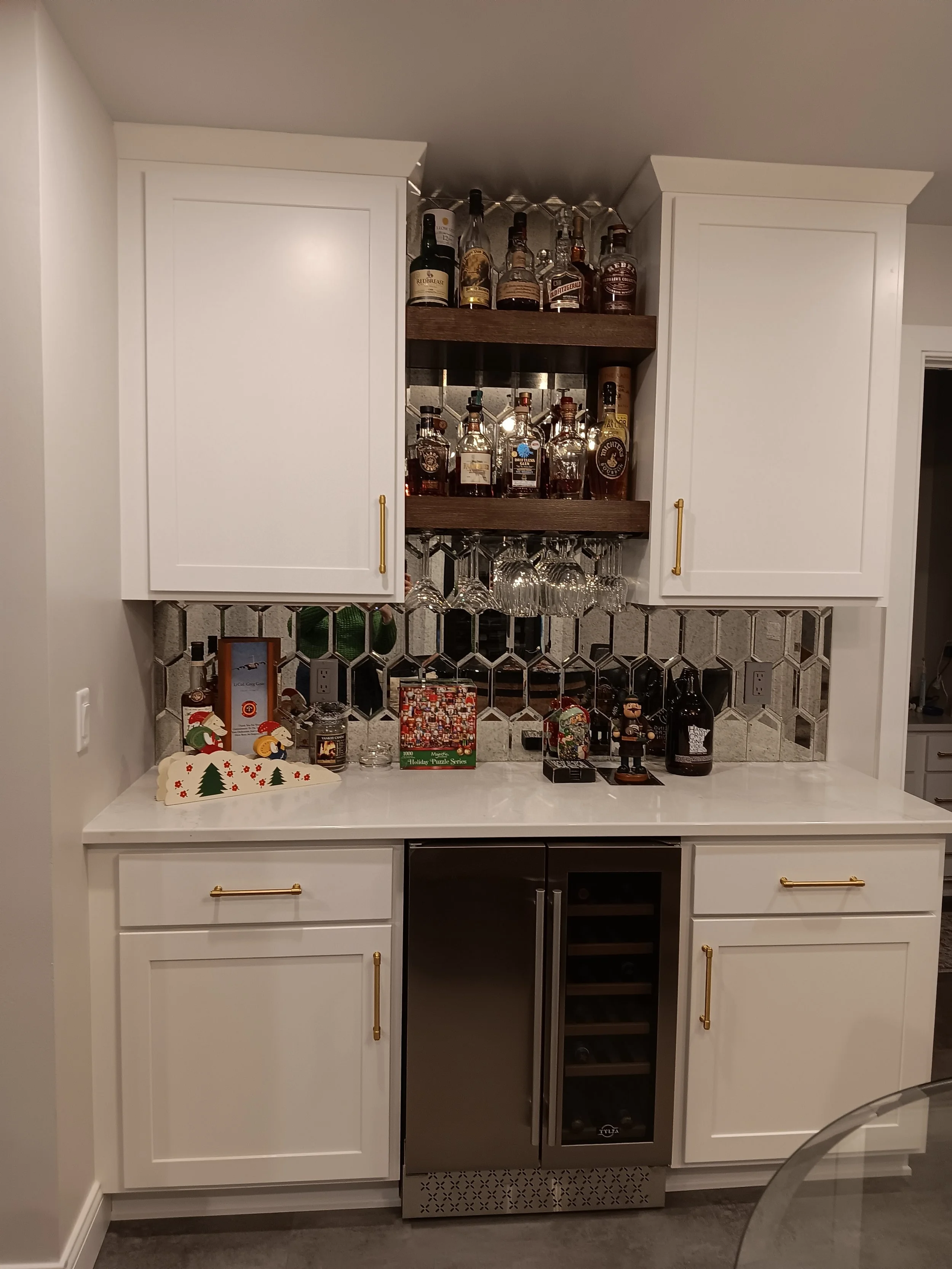 Home bar with white cabinets, a wine cooler, and a mirrored tile backsplash, decorated with holiday-themed items and liquor bottles.
