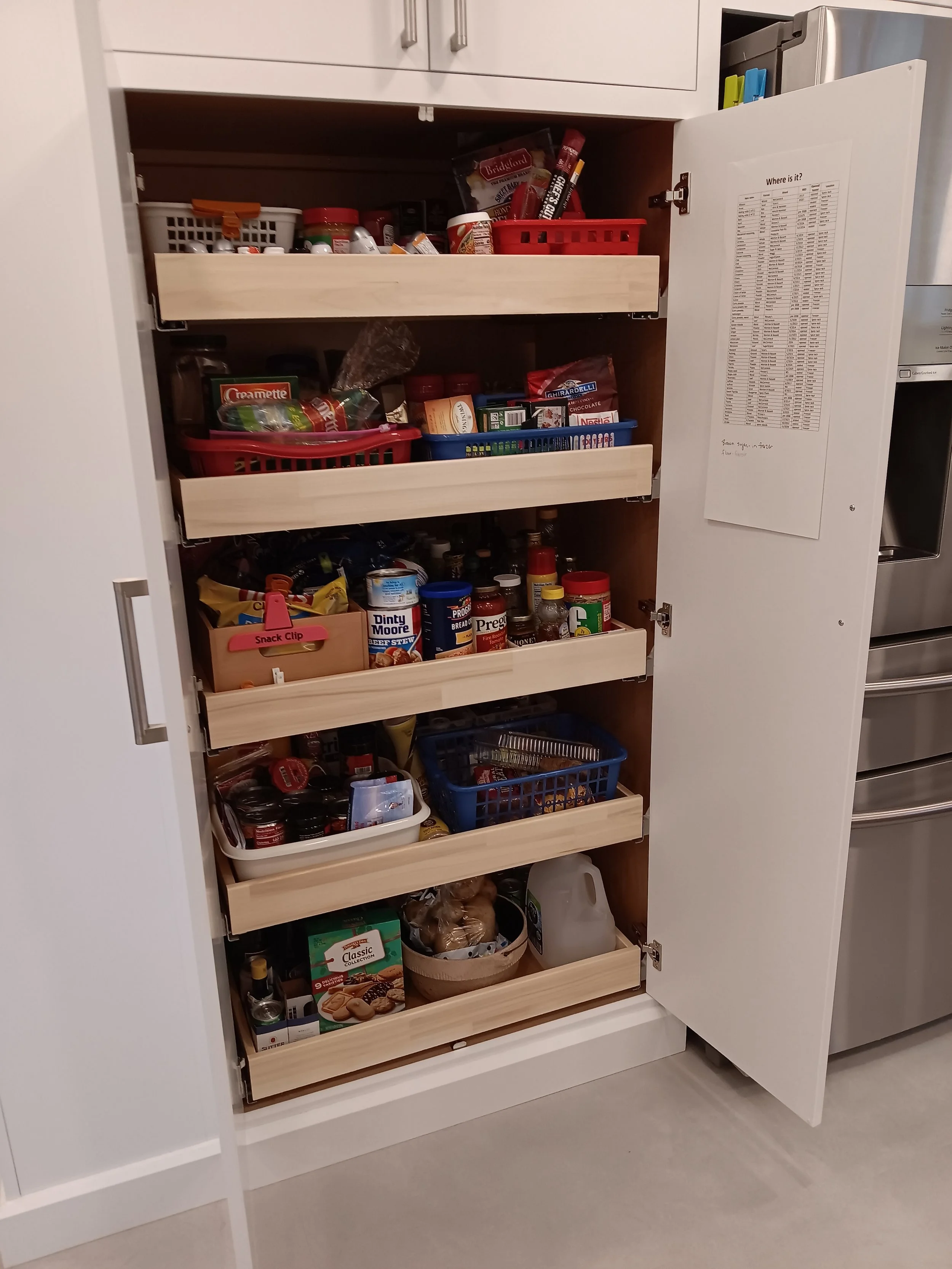Open kitchen pantry with multiple shelves filled with food and spices, some items stored in containers and baskets.