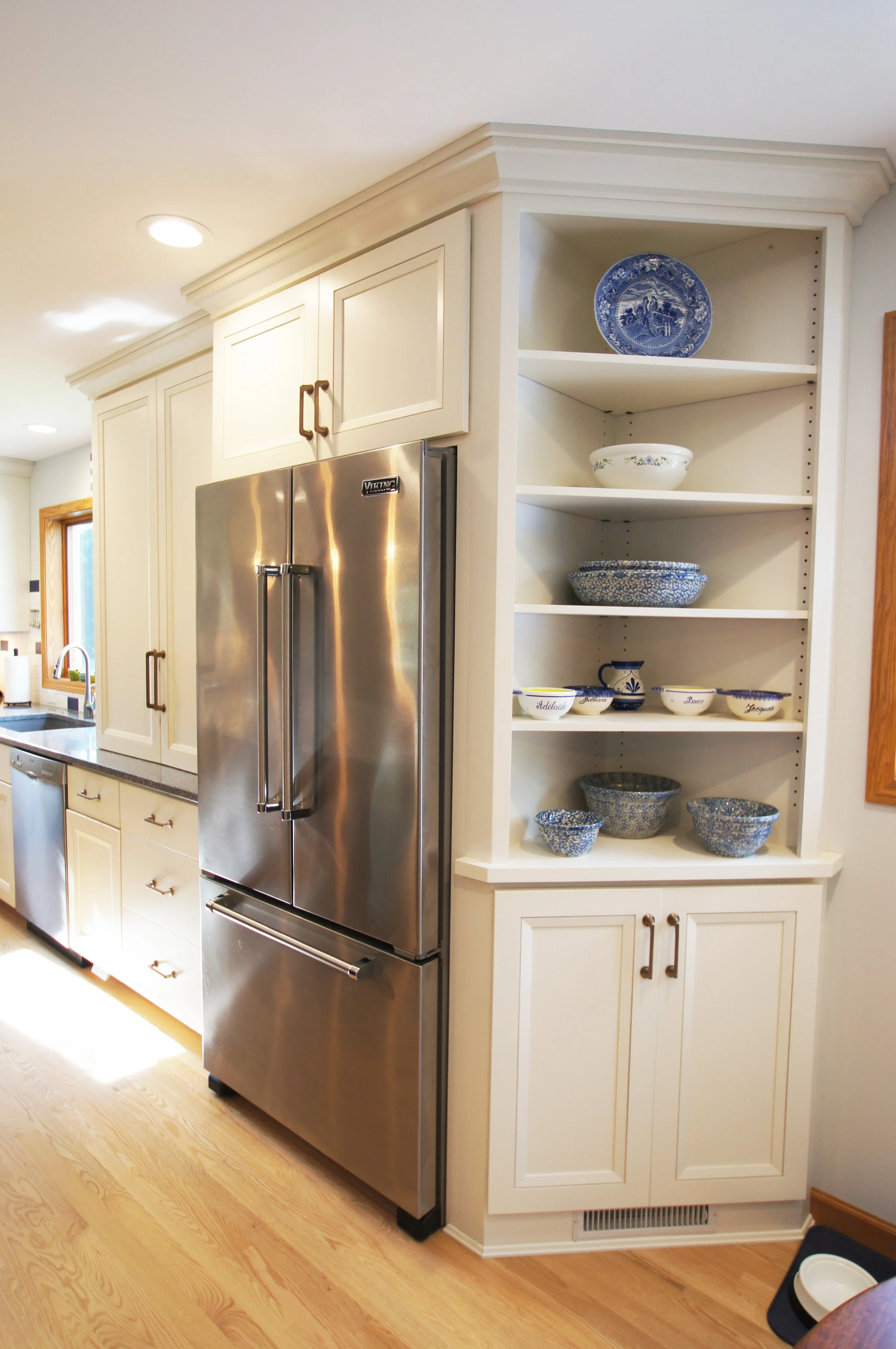 Kitchen with open shelving displaying blue and white bowls and dishes, next to a stainless steel refrigerator.