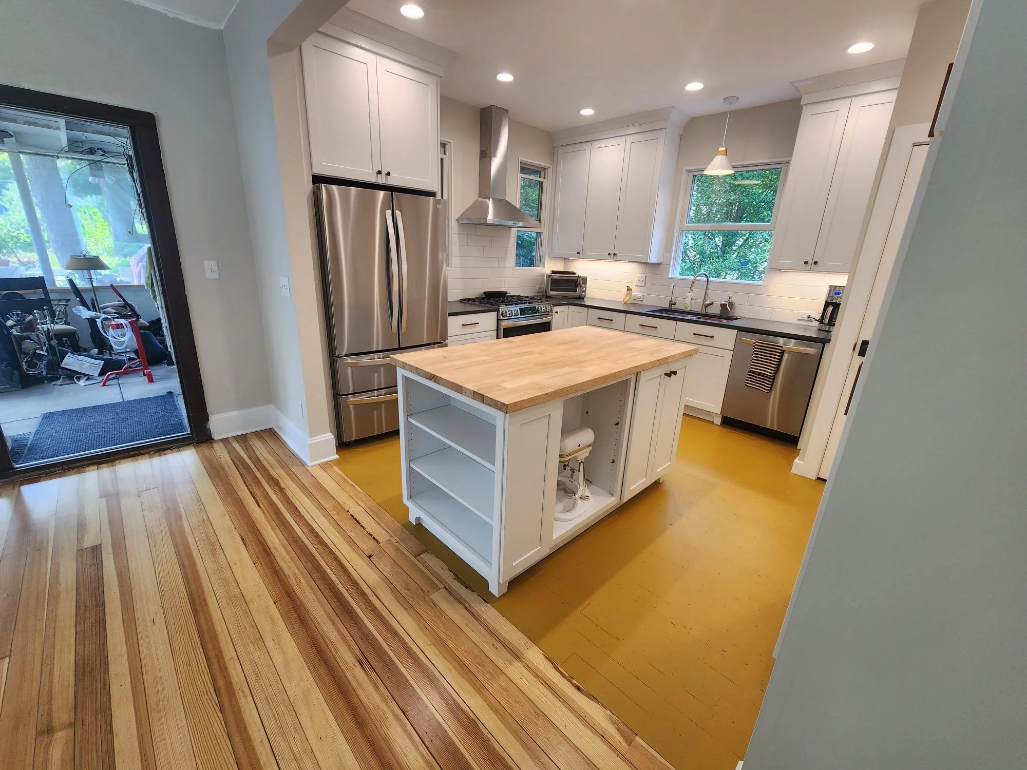 Modern kitchen with white cabinets, stainless steel appliances, a small island with a butcher block top, and hardwood flooring.
