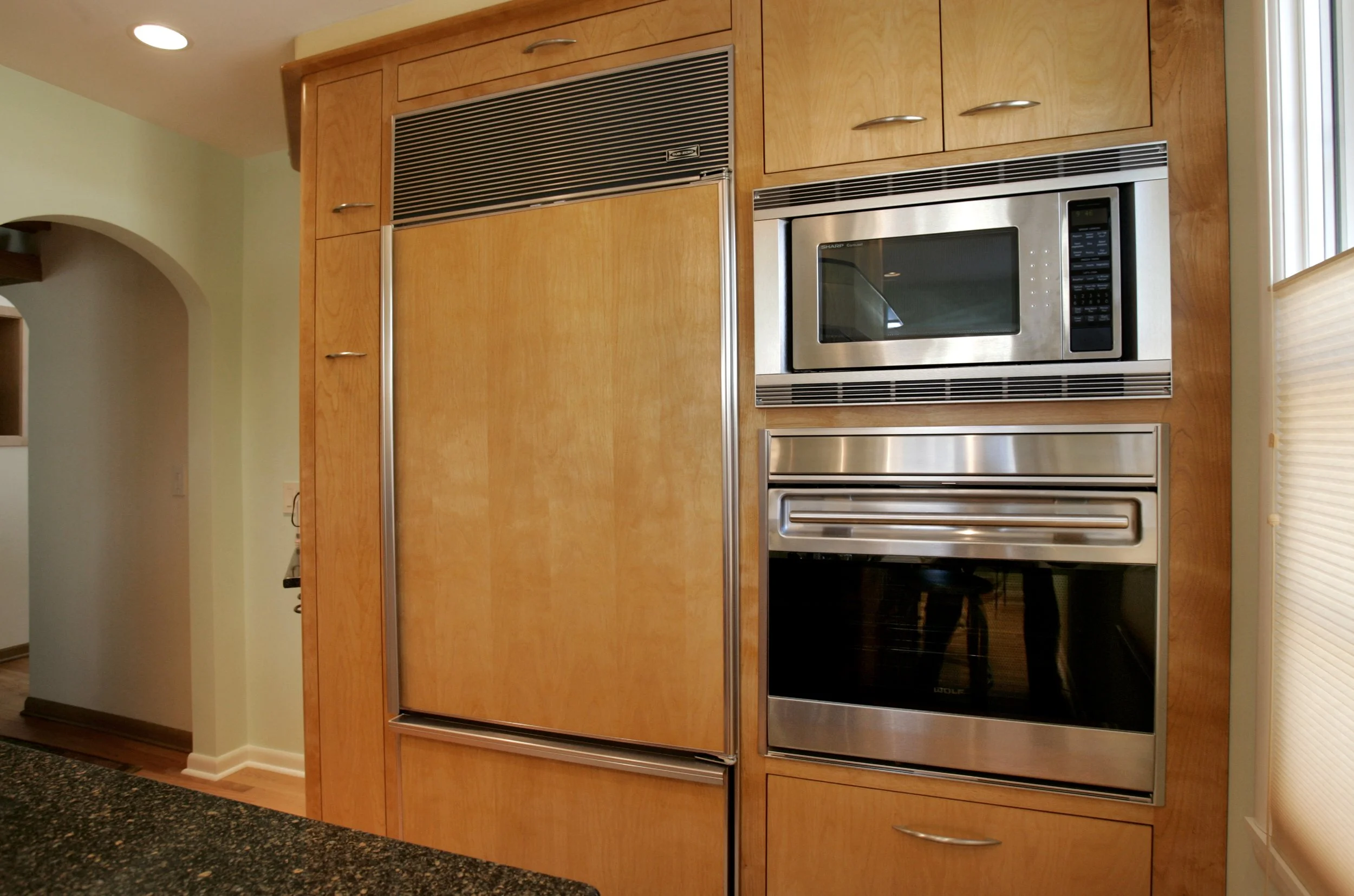 Kitchen with wooden cabinets, built-in microwave, oven, and refrigerator, with a window on the right side.